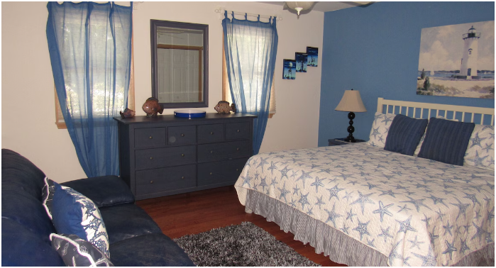 Beach-themed bedroom with blue walls, starfish-patterned bedding, and nautical decor, including a lighthouse painting and seashells on dresser.