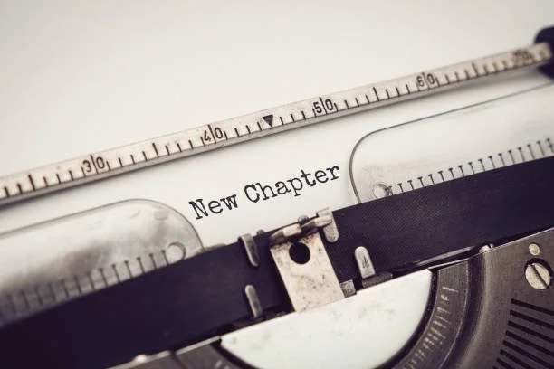 Close-up of a vintage typewriter with a piece of paper inserted that reads 'New Chapter,' accompanied by a ruler-shaped object above.