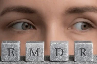 Close-up of a person's eyes above four Scrabble tiles spelling 'EMDR'.
