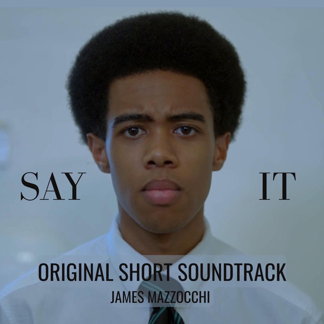 Close-up of a young man with an afro hairstyle, wearing a white shirt and striped tie, looking serious, with text "SAY IT" and "ORIGINAL SHORT SOUNDTRACK JAMES MAZZOCCHI" overlaid.