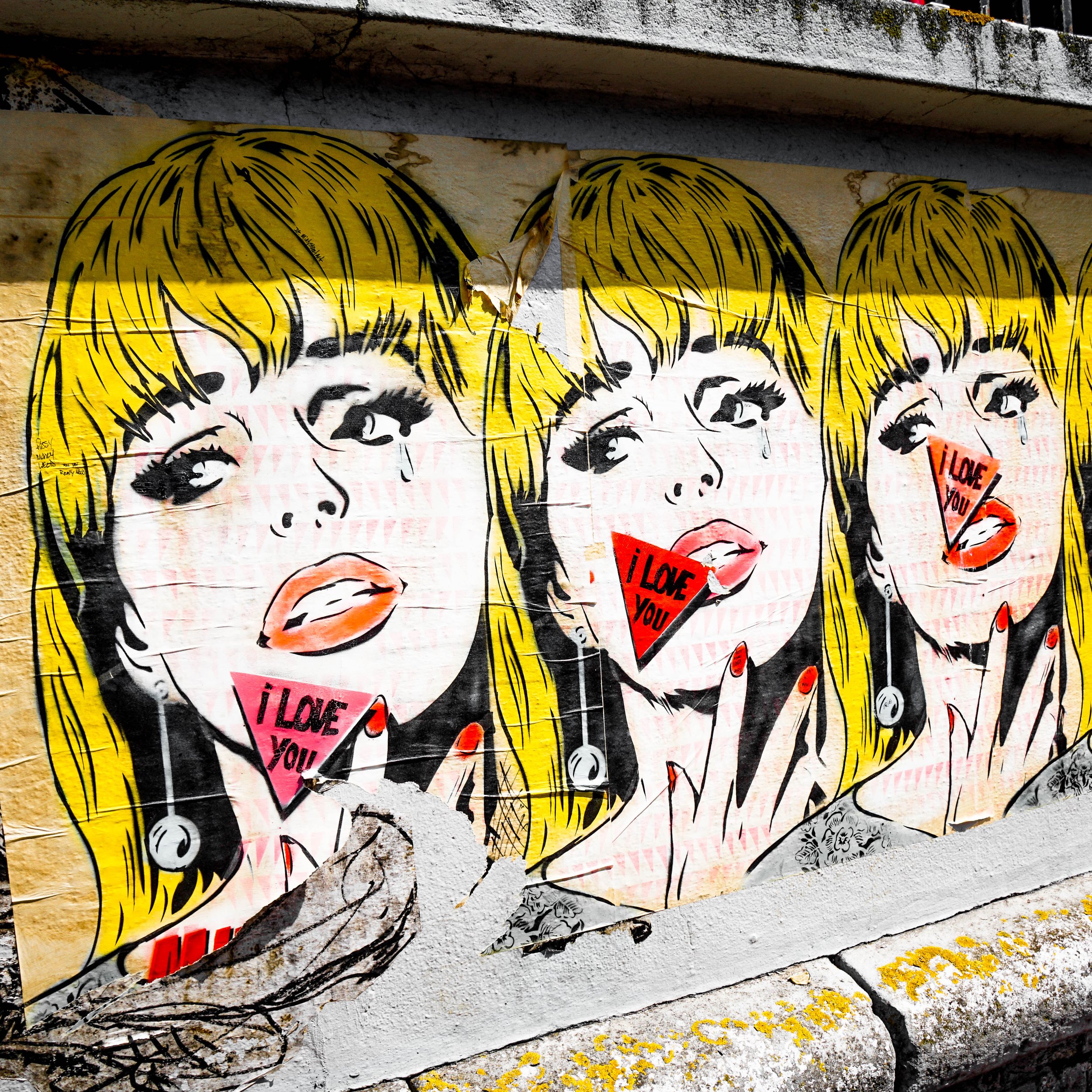 Street art in Brighton. A woman's face repeated three times. Yellow hair, red lips. Triangular signs saying I Love You.