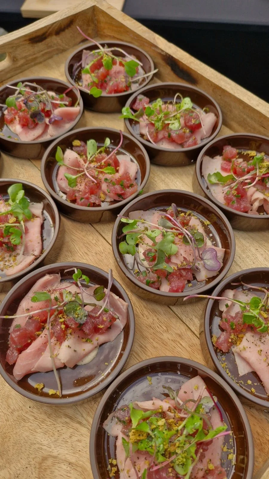 Voorgerecht Vitello, makreel, verse tonijn met groene kruiden in kleine bakkertjes op een houten tafel.