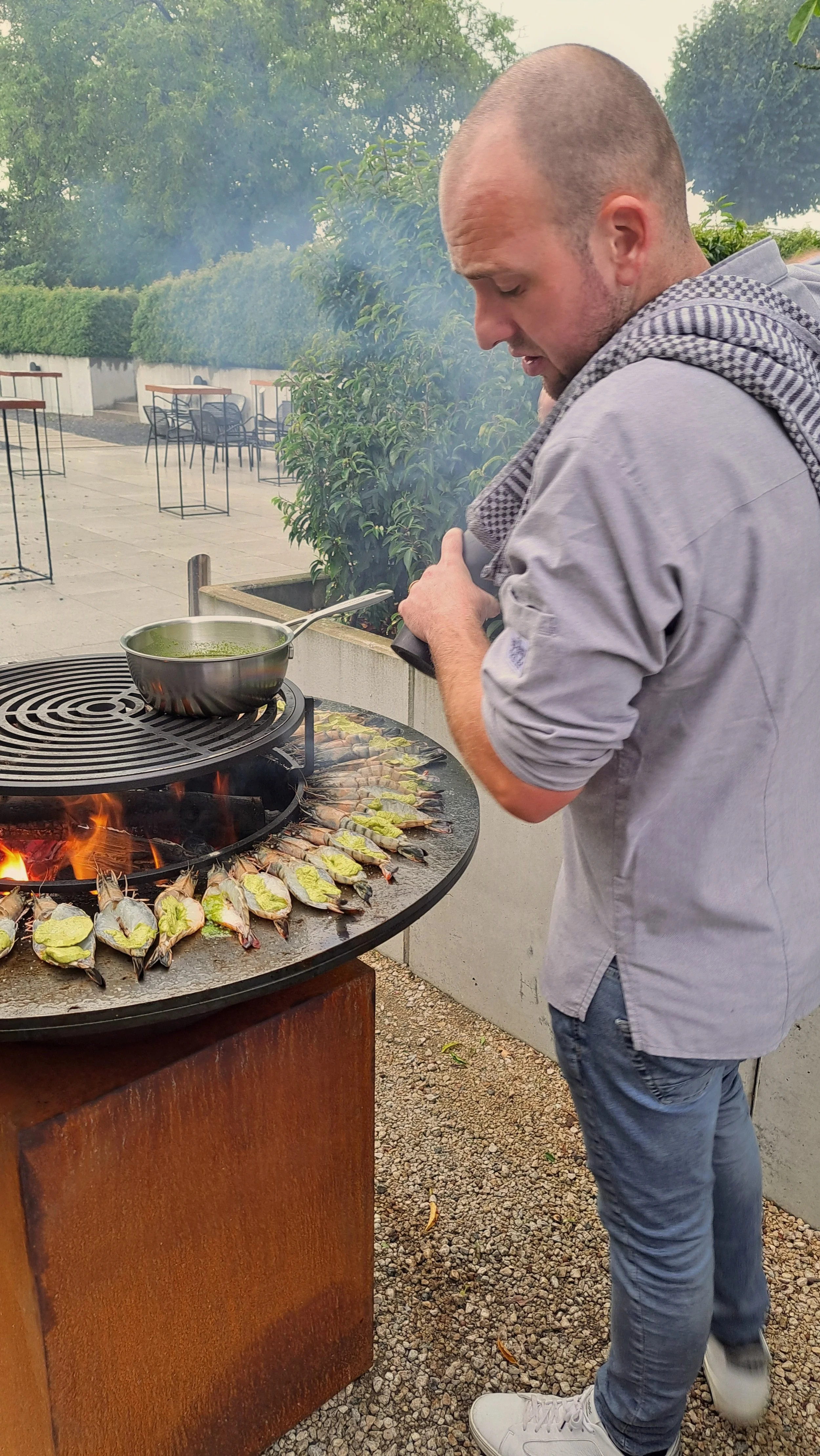 Man die gamba's op een Ofyr grillt en peper over de gamba's strooit.
