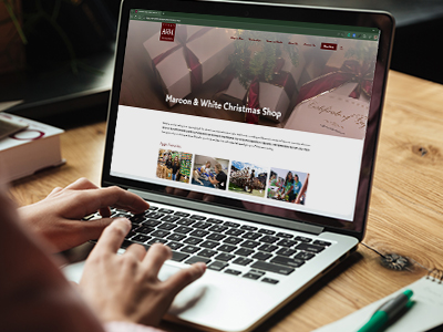 A woman's hands hover over a laptop open to a "Maroon & White Christmas Shop" page.