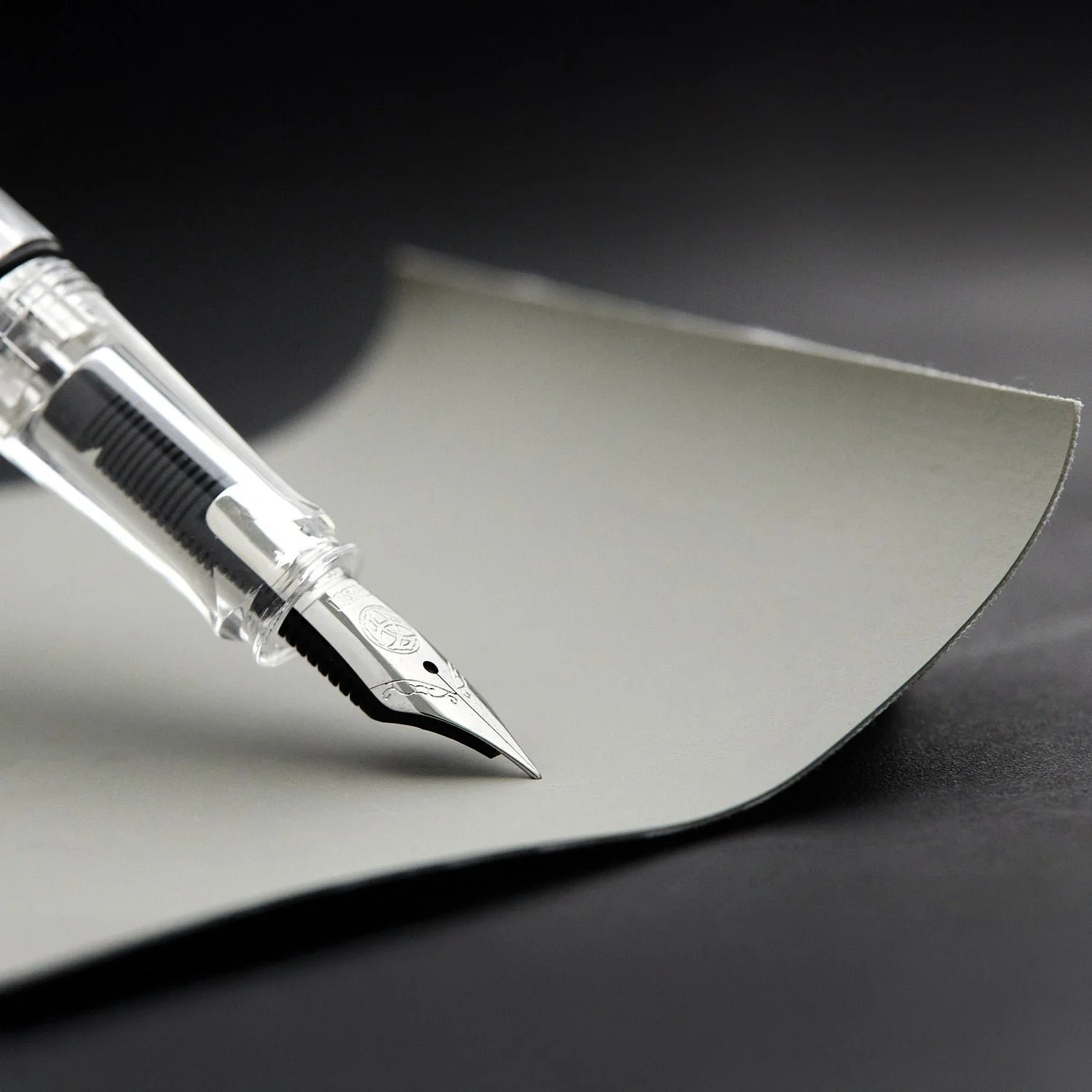Close-up of a fountain pen resting on a blank sheet of paper with a dark background.