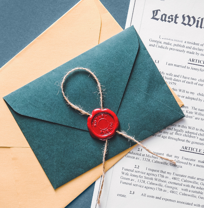 A teal envelope sealed with red wax and tied with twine, placed on top of a yellow envelope and a document or will.