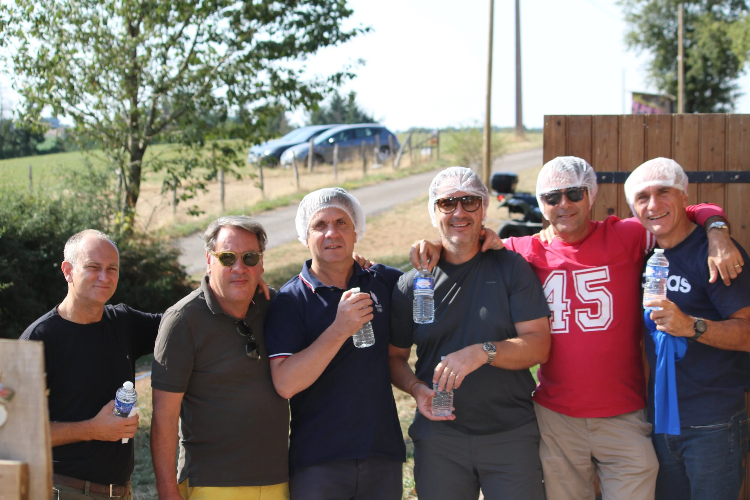 Groupe de sept hommes souriants posant ensemble lors d'une activité en extérieur, certains portant des bonnets en plastique. 