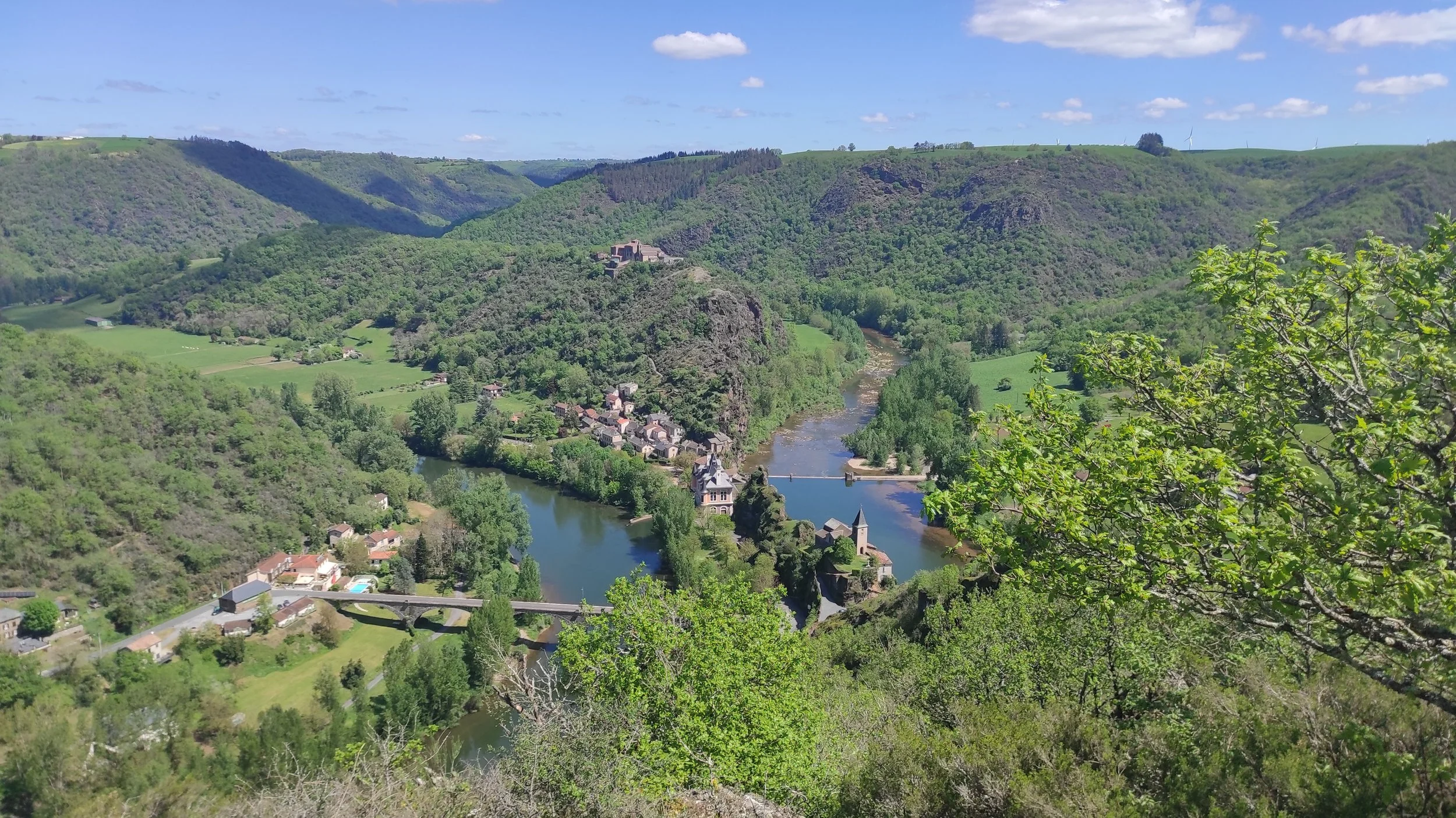 Paysage verdoyant avec une rivière serpentant à travers une vallée, entourée de collines boisées et de petits villages.