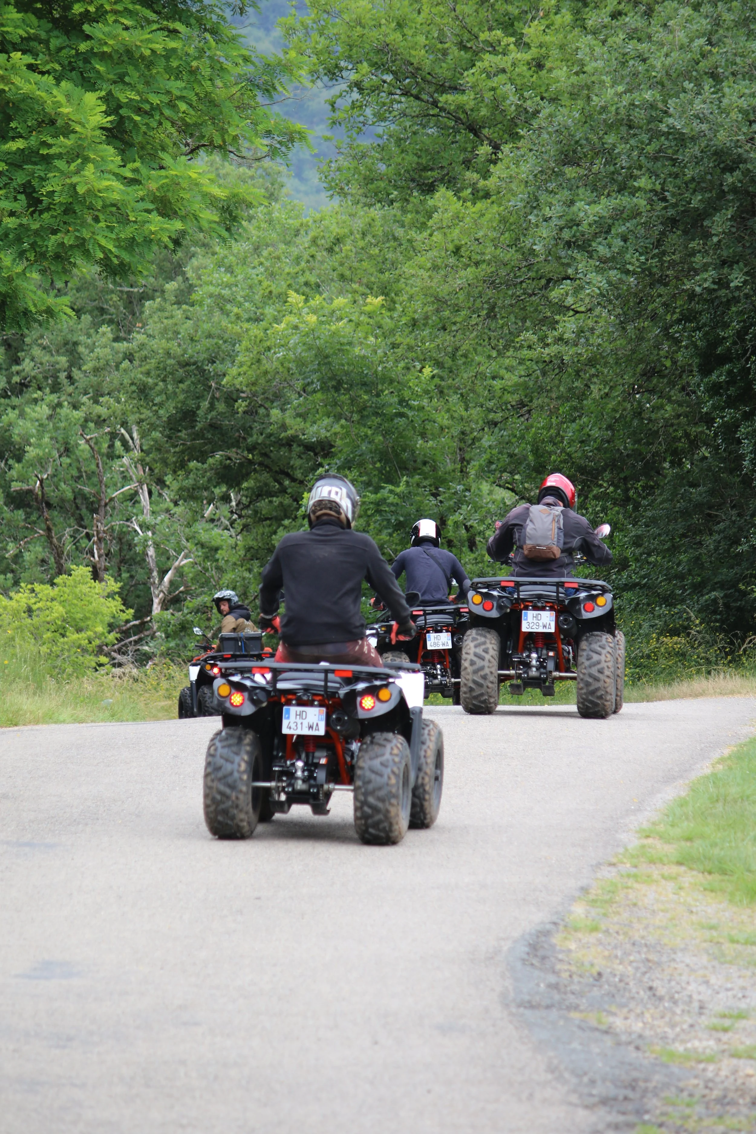 Groupe de personnes en casque conduisant des quads sur un chemin dans une forêt verte.