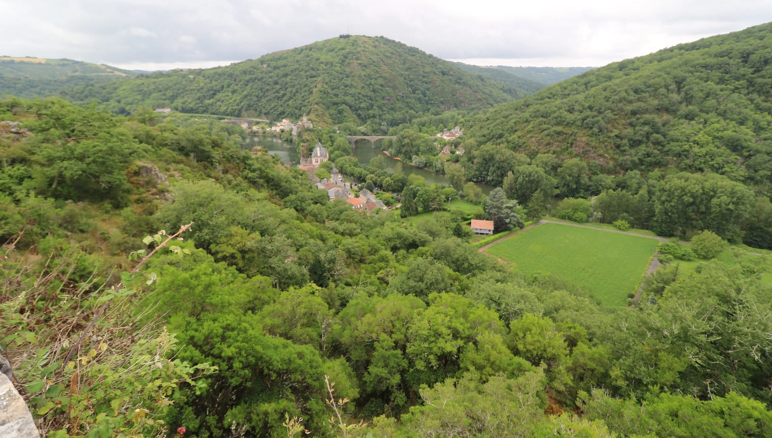 Paysage verdoyant avec une rivière traversant un village entouré de collines boisées et une zone culturale