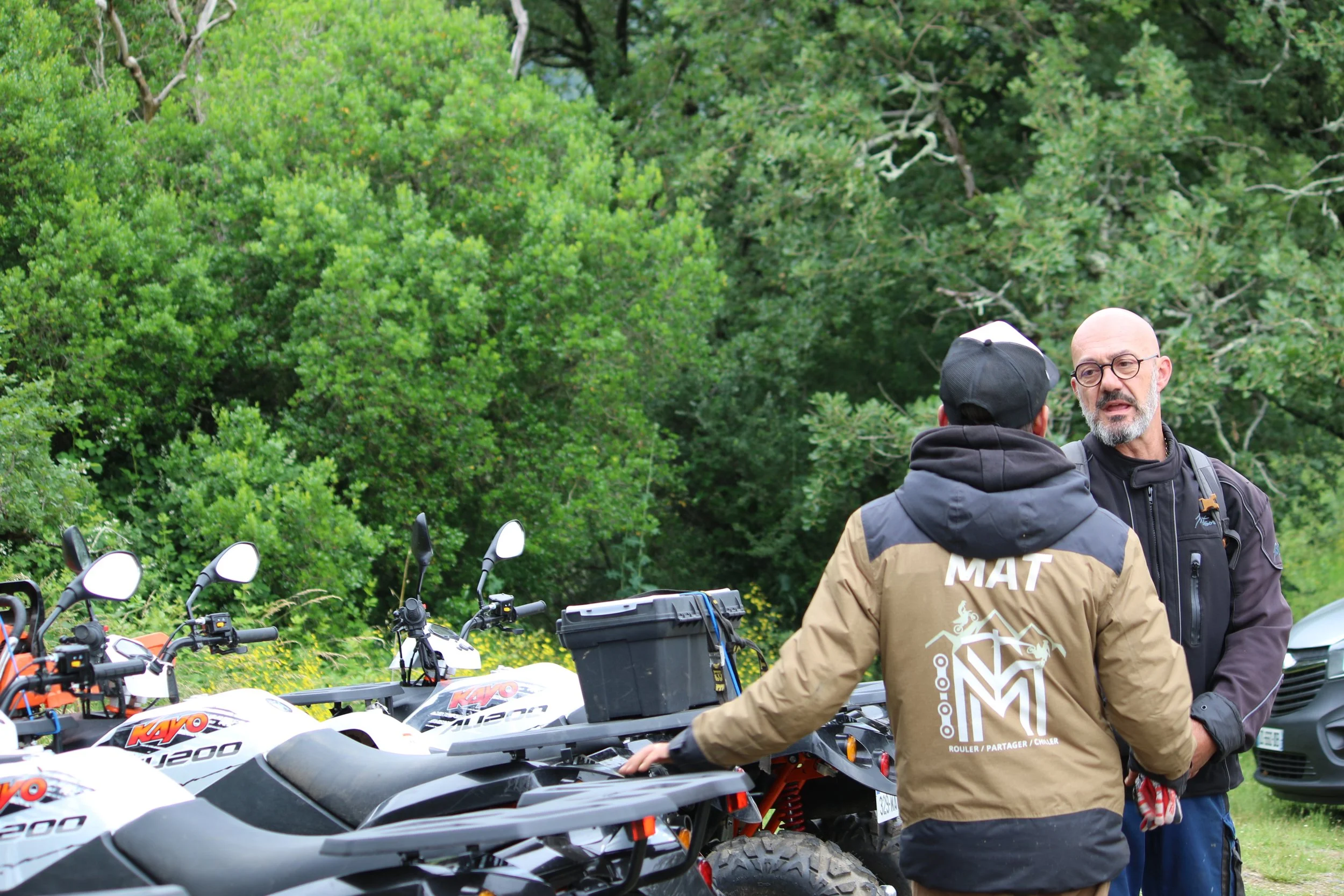 Deux hommes parlant à côté de quads dans un environnement boisée.
