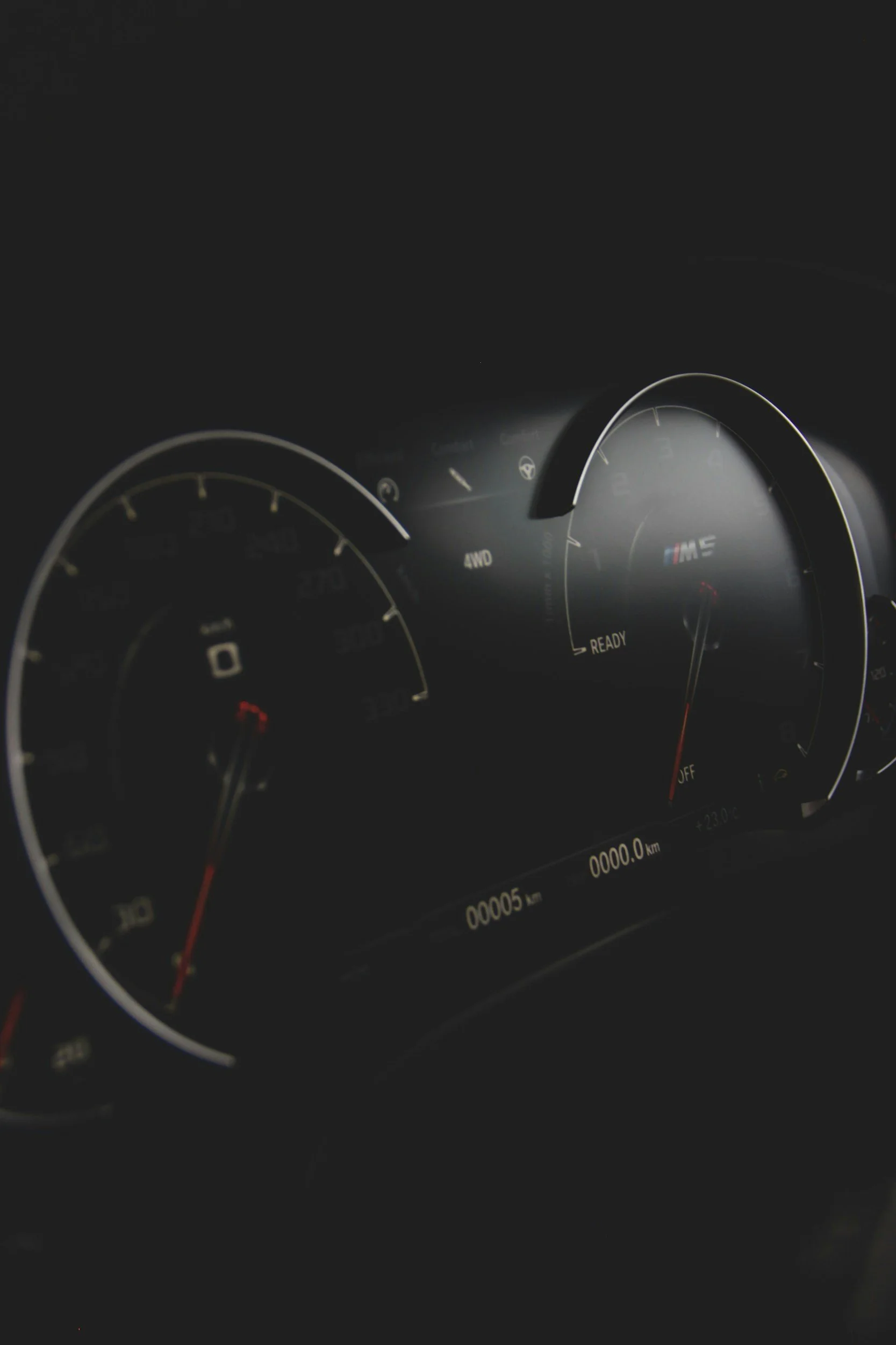 Close-up of a car's dashboard with illuminated speedometer and tachometer, showing the car is stationary with 0 km/h and 0 rpm.