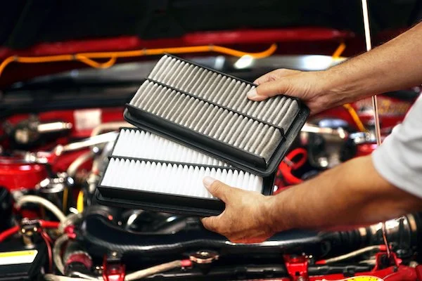 Person holding two car air filters over engine bay with red components.
