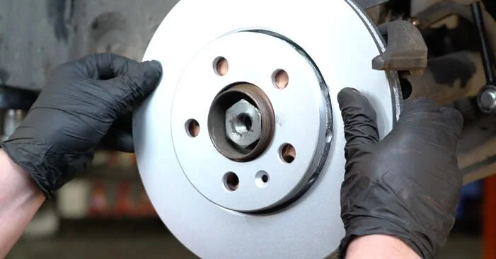 Close-up of a person's hands in black gloves holding a car brake rotor in a workshop.