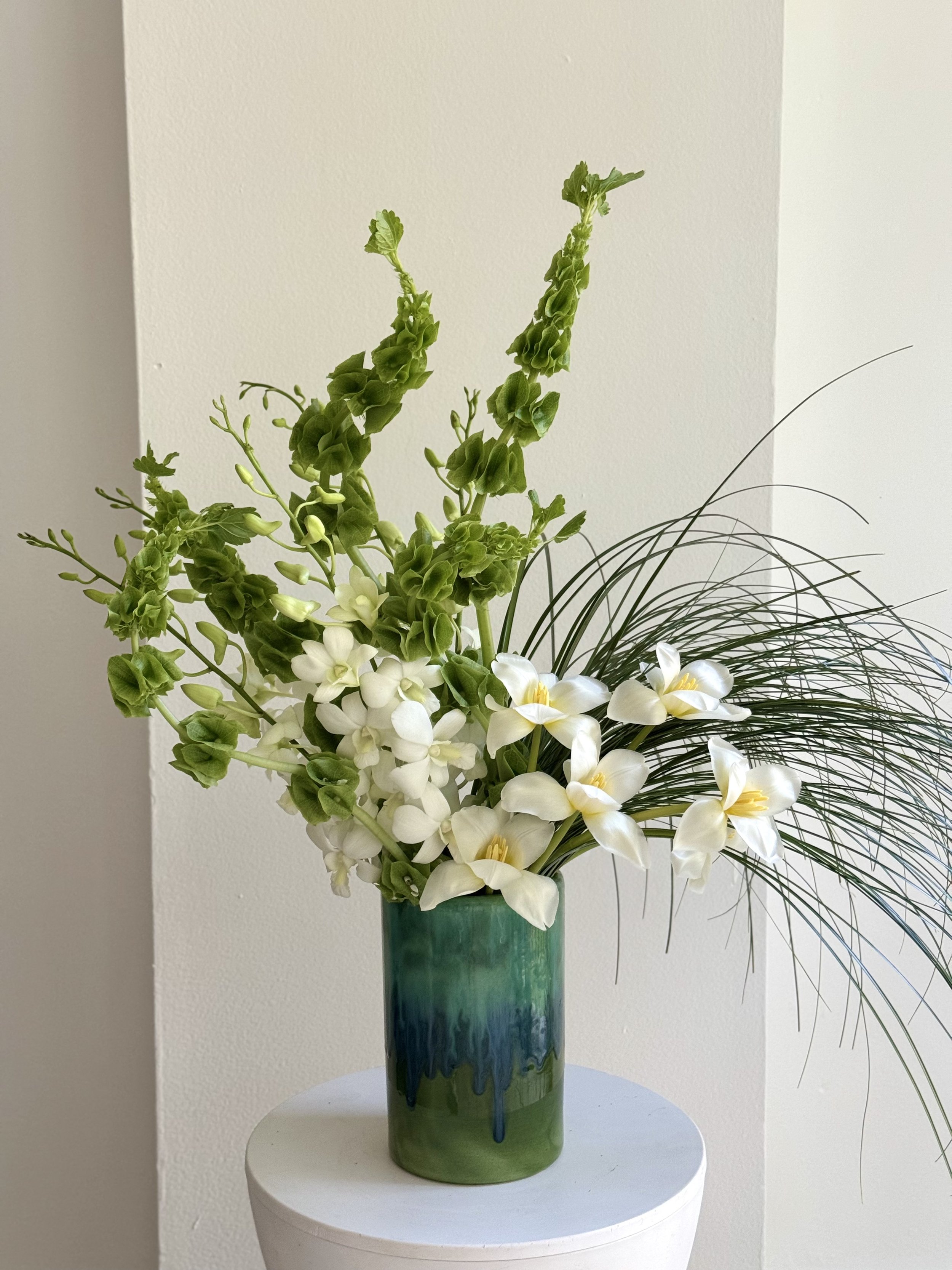  Constructed arrangement with green bells of Ireland, white orchids, and bear grass in a green ceramic vase 