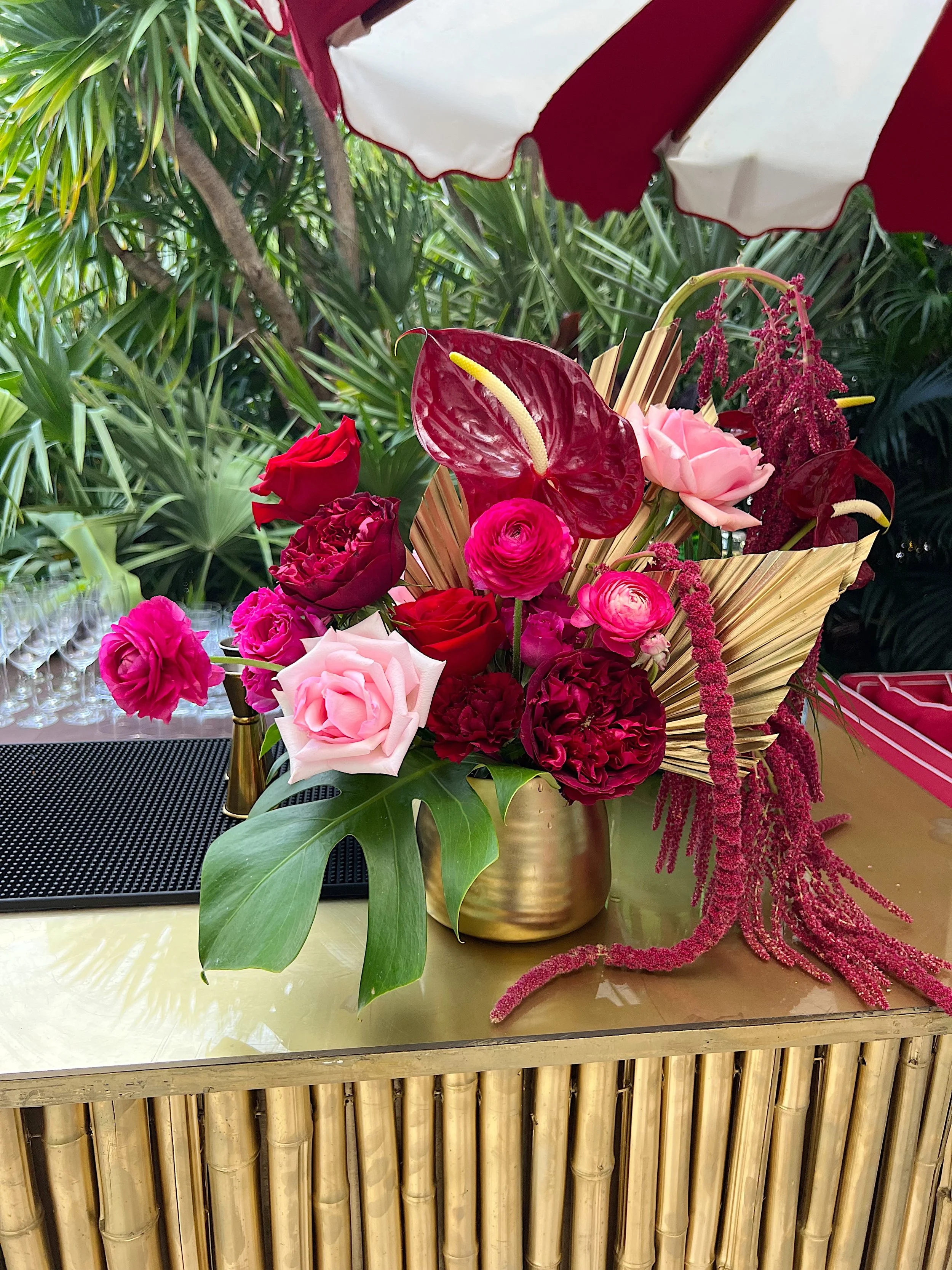  burgundy anthurium and pink rose arrangement in gold vase with tropical leaves 