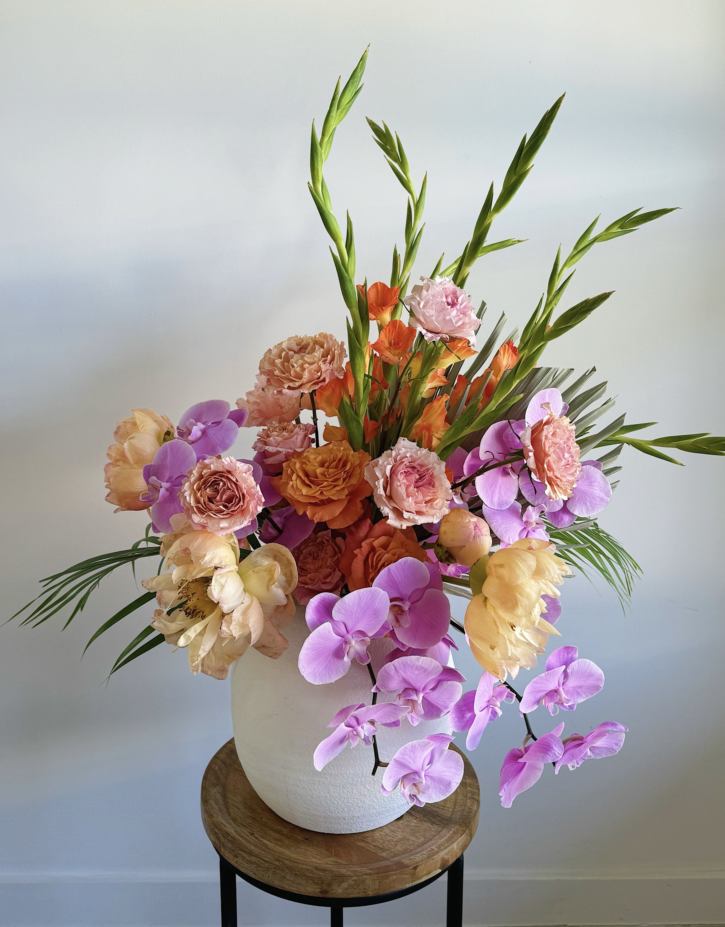 A large bouquet of colorful flowers in a white vase on a small wooden side table