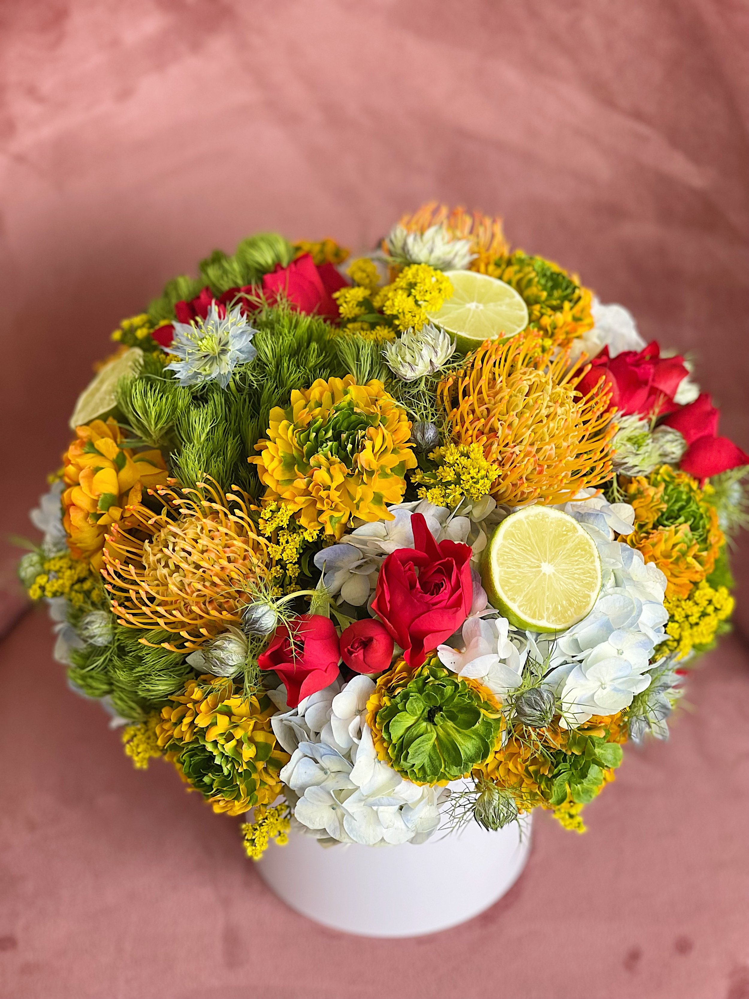 Colorful flower bouquet with red roses, white hydrangeas, yellow and orange flowers, and slices of lemon in a white vase.