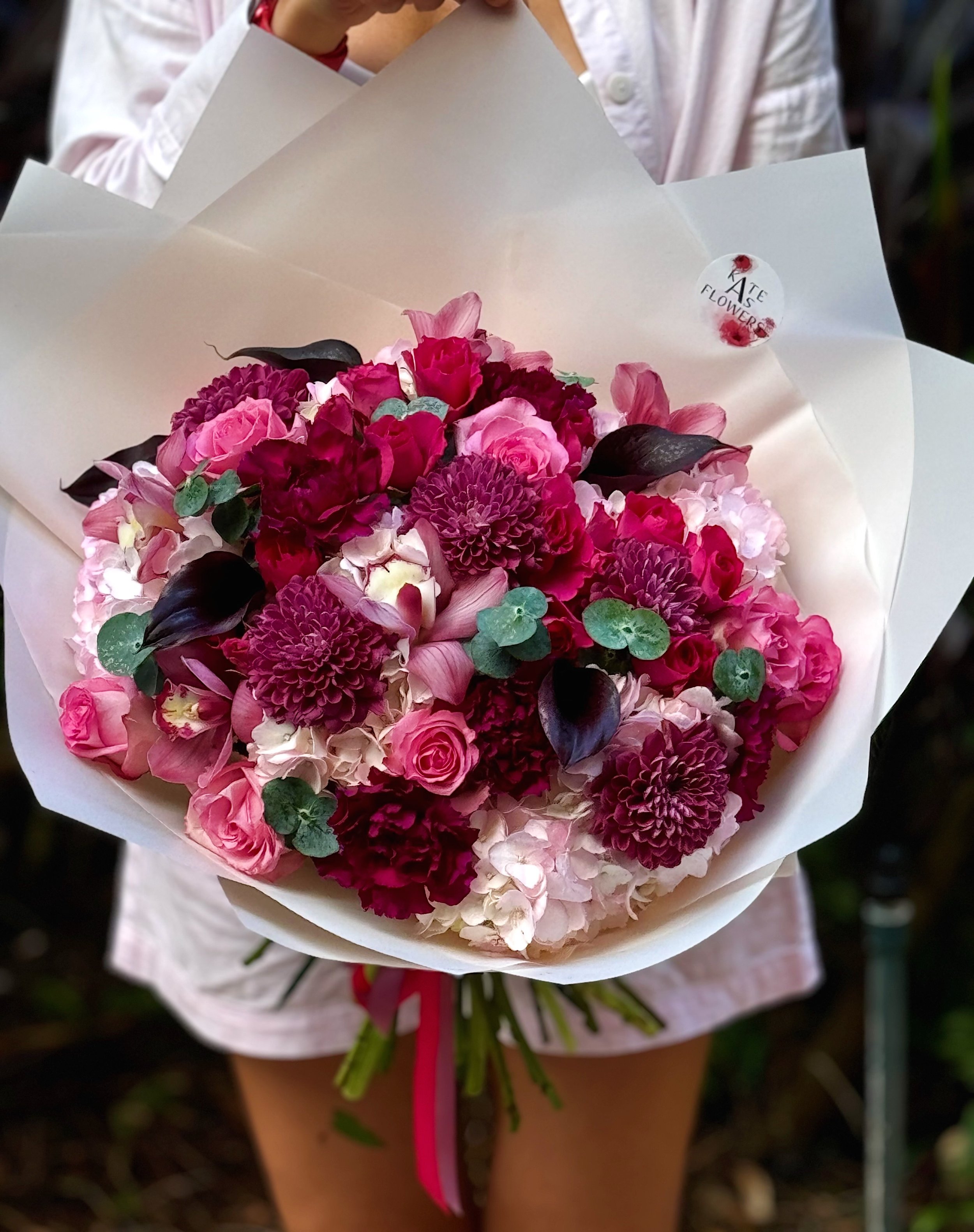 Person holding a large bouquet of pink, purple, and white flowers wrapped in white paper.