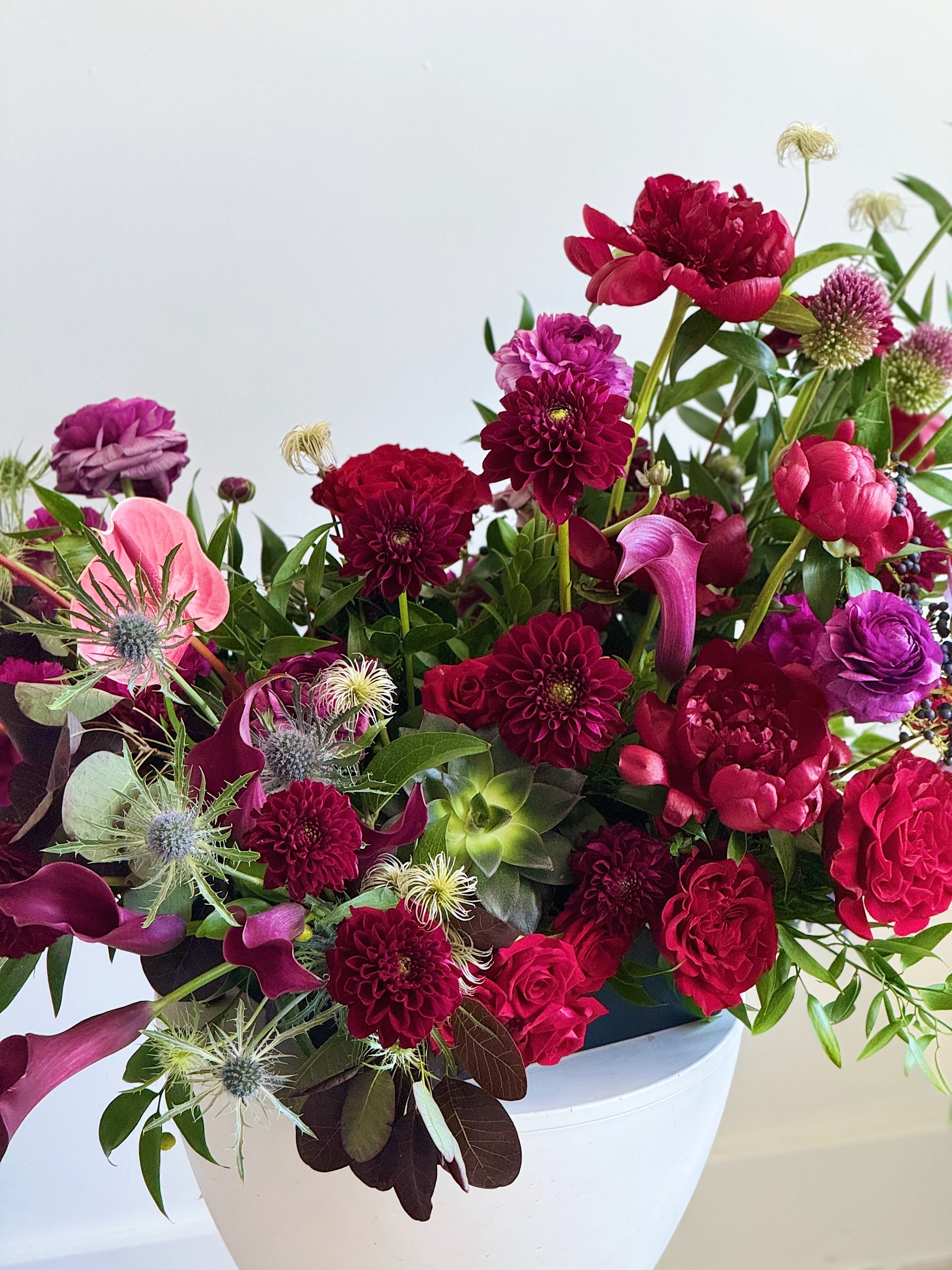 A colorful bouquet of various pink, purple, and red flowers in a white vase.