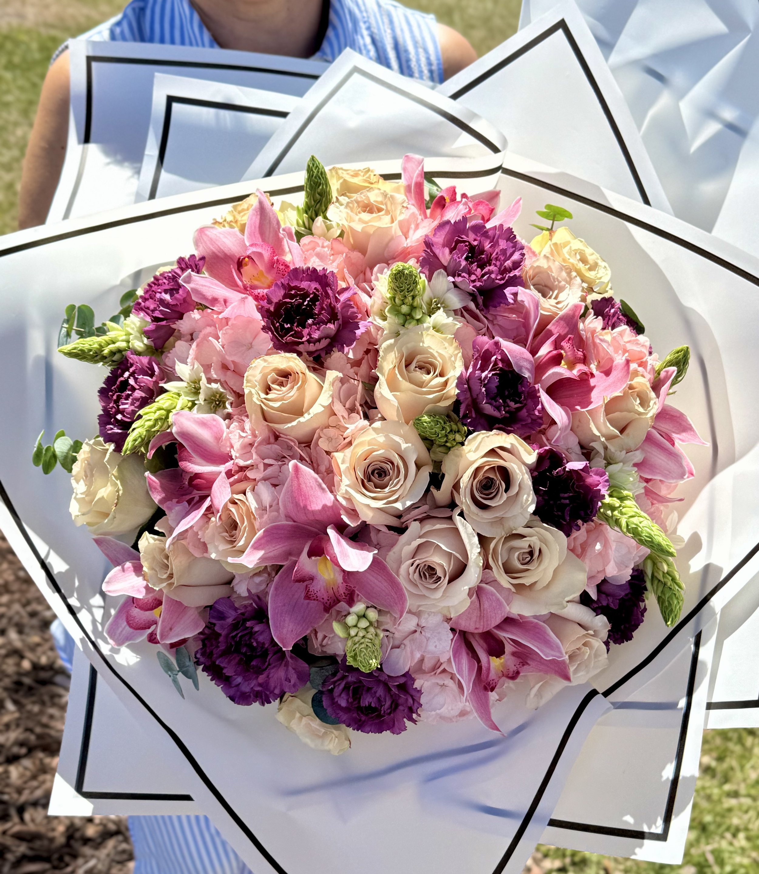 A large bouquet of pink, white, and purple flowers including roses, orchids, and other blooms, wrapped in white decorative paper.