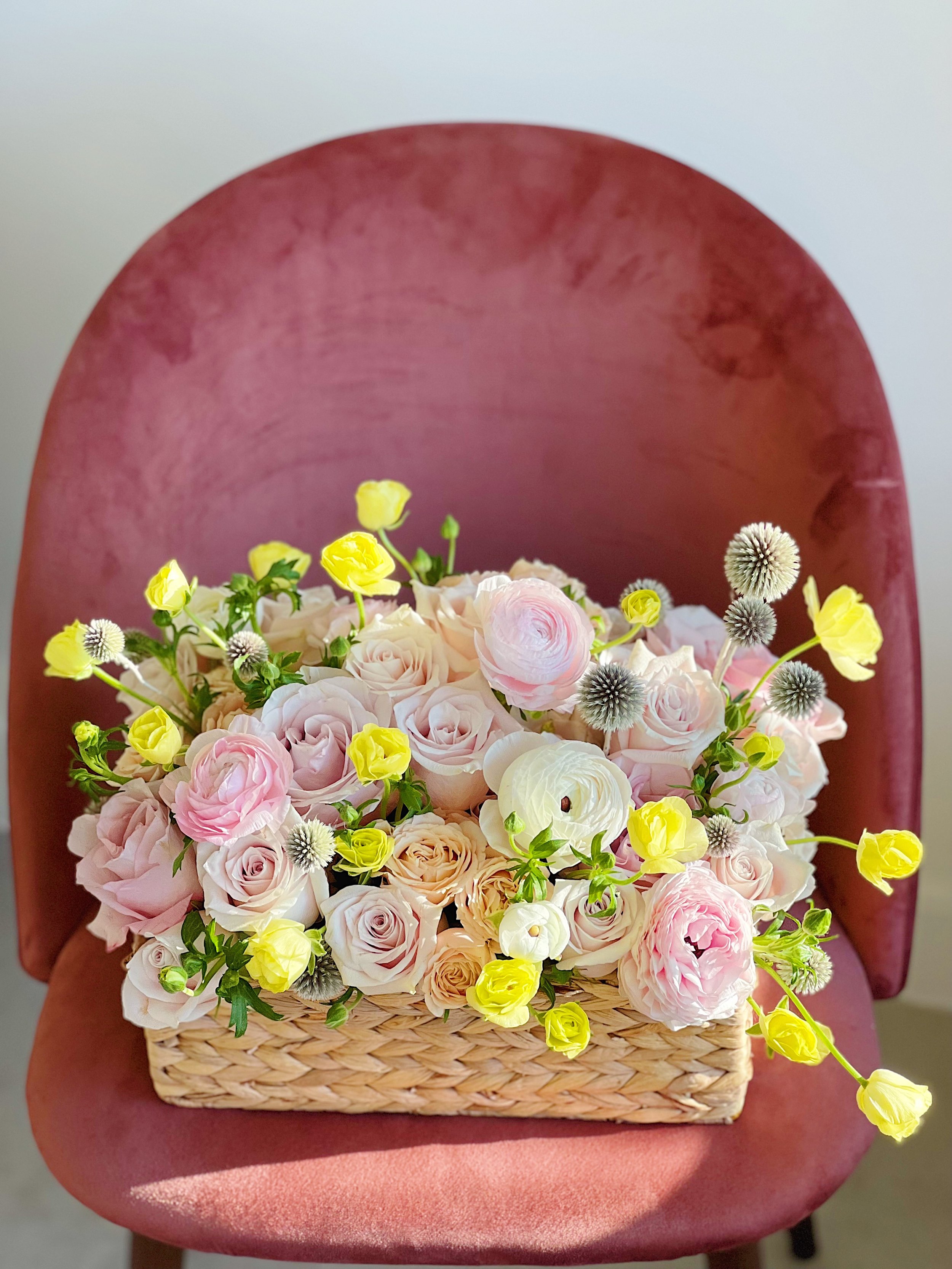 A basket of pink, white, and yellow flowers placed on a pink upholstered chair.