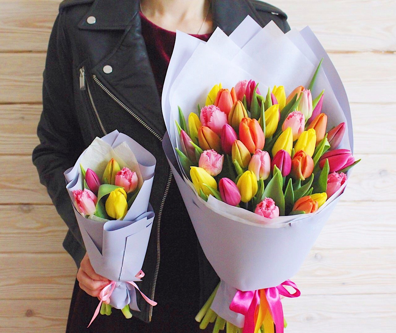 A person holding two bouquets of colorful tulips in front of a wooden wall.