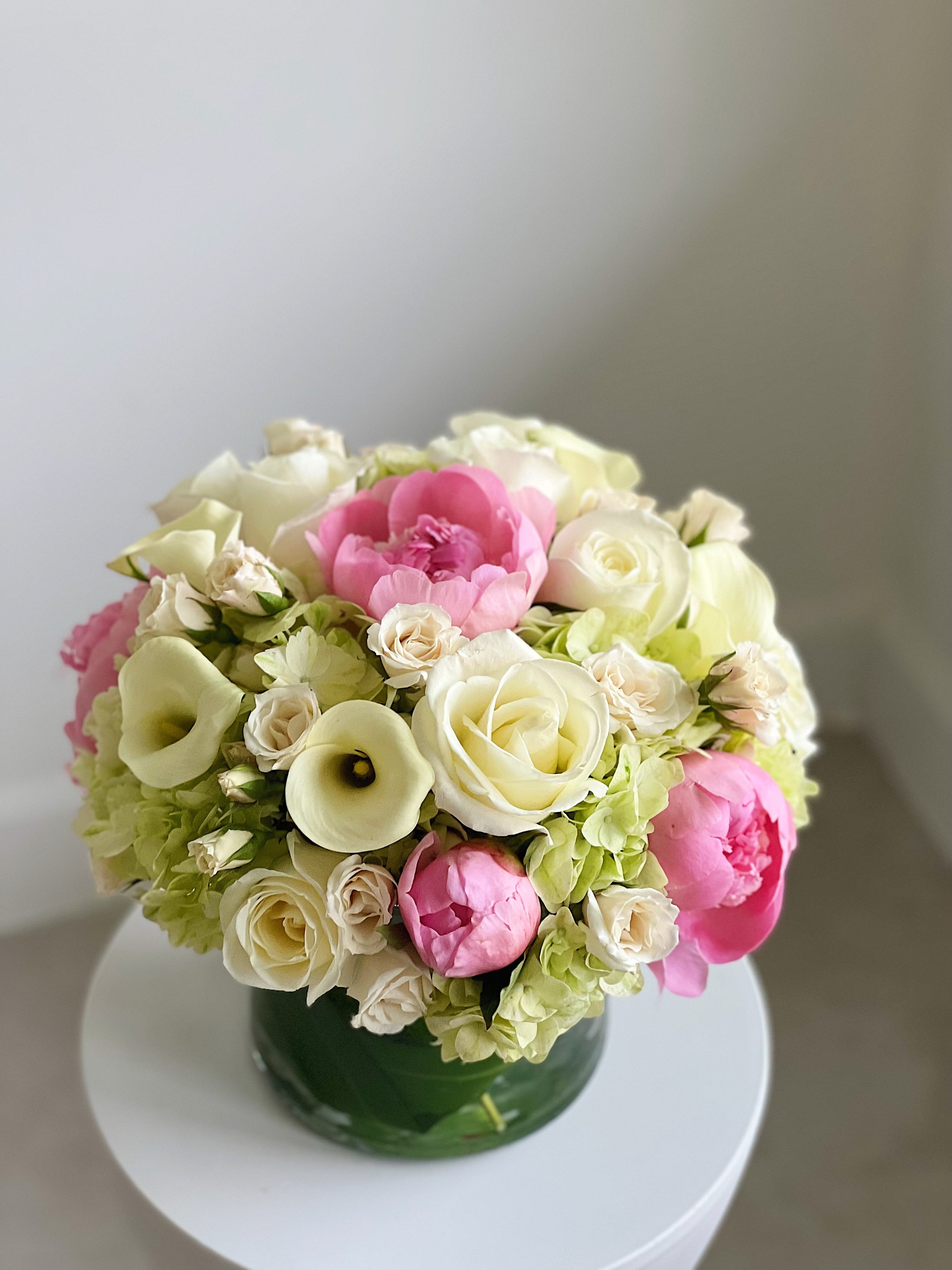A bouquet of white and pink flowers in a green vase on a white table.