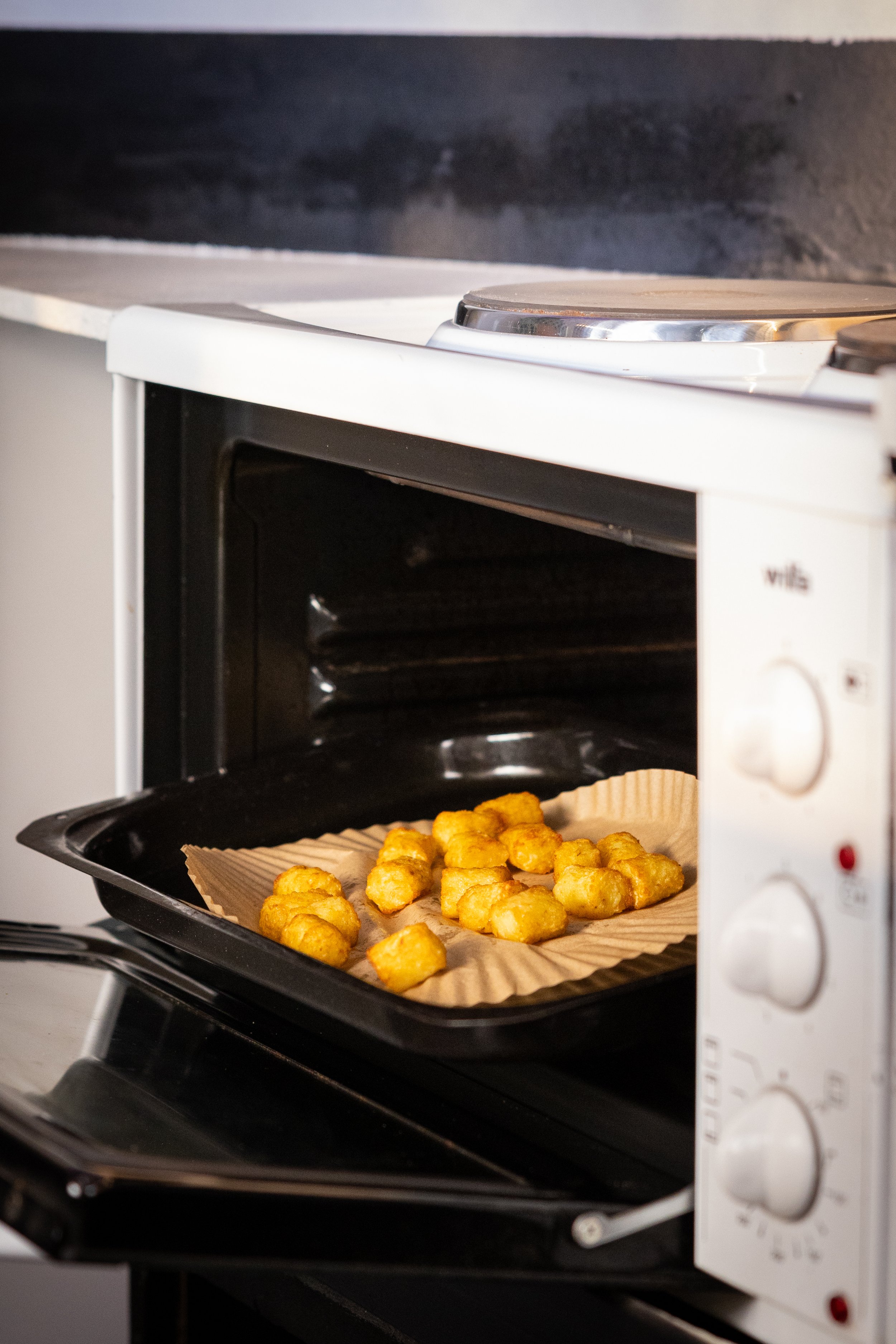 Tater tots baking in a toaster oven on a baking sheet lined with parchment paper.