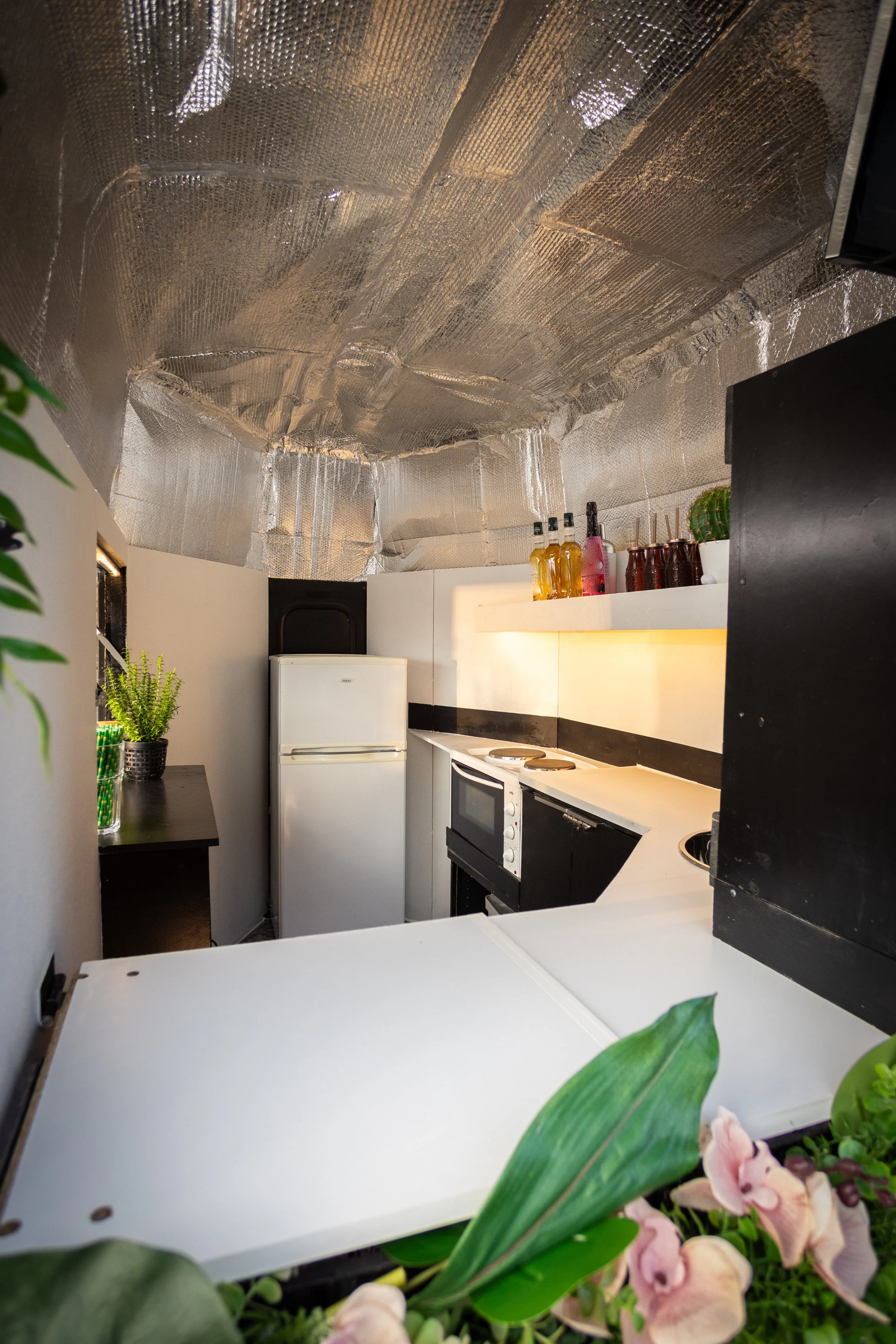 Small kitchen with white appliances, black and white cabinetry, a mirrored ceiling, and some plants and decorative items.