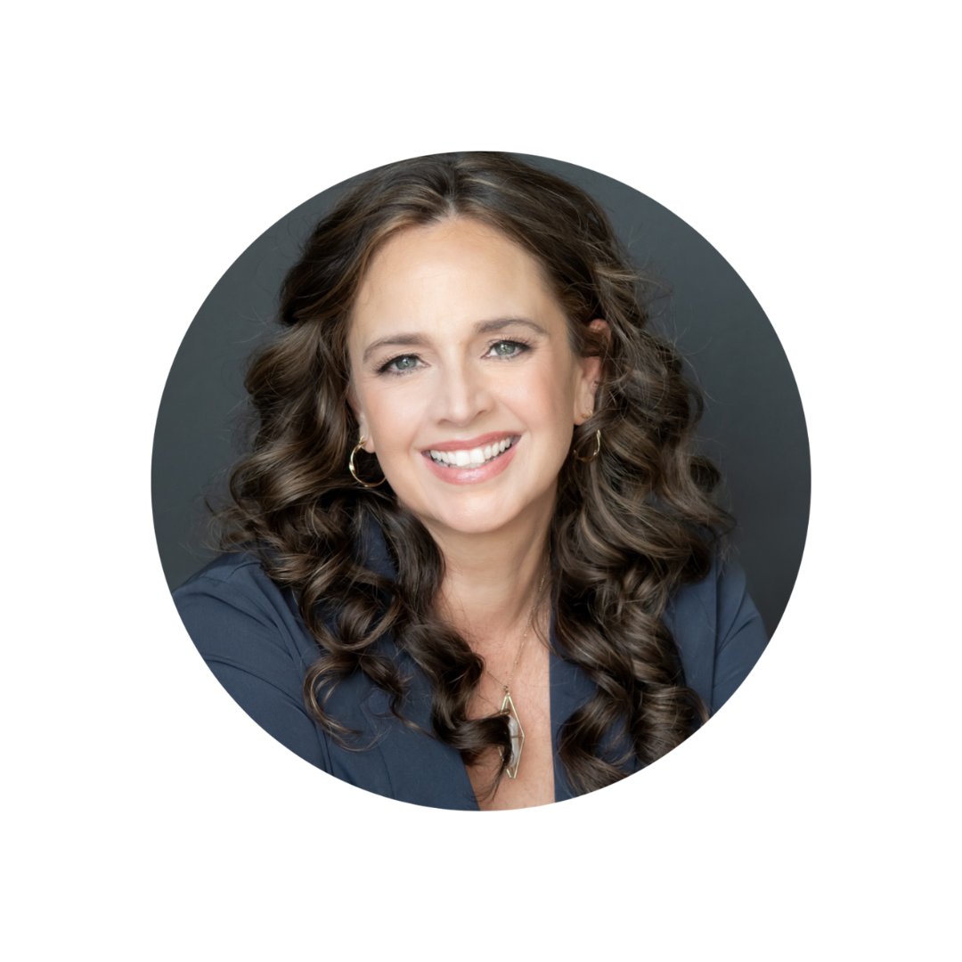 A woman with long, curly brown hair, blue eyes, and earrings, smiling and wearing a dark blue blazer against a dark background.
