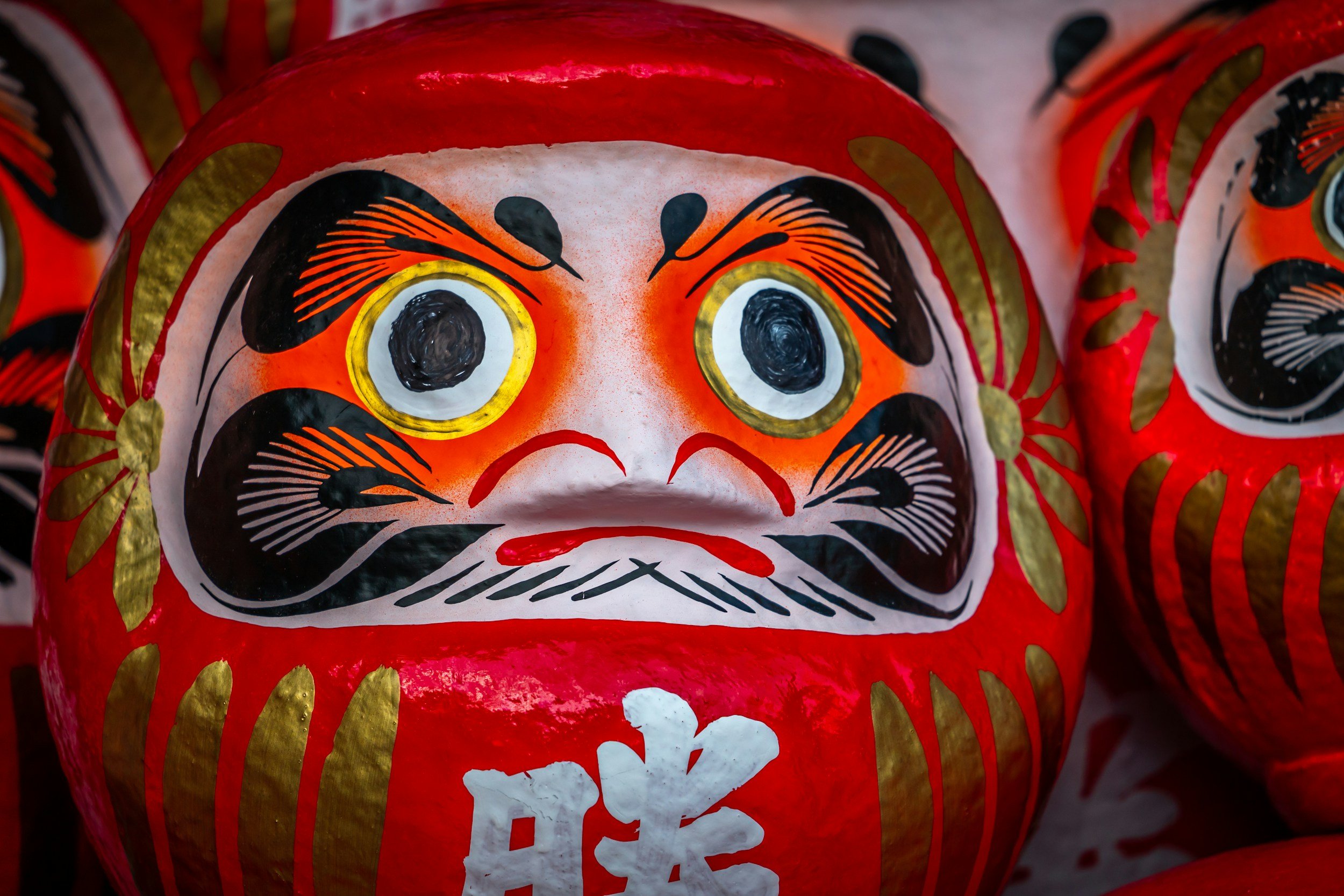 A close-up shot of red Daruma doll, with focus on its hand-drawn eyes.