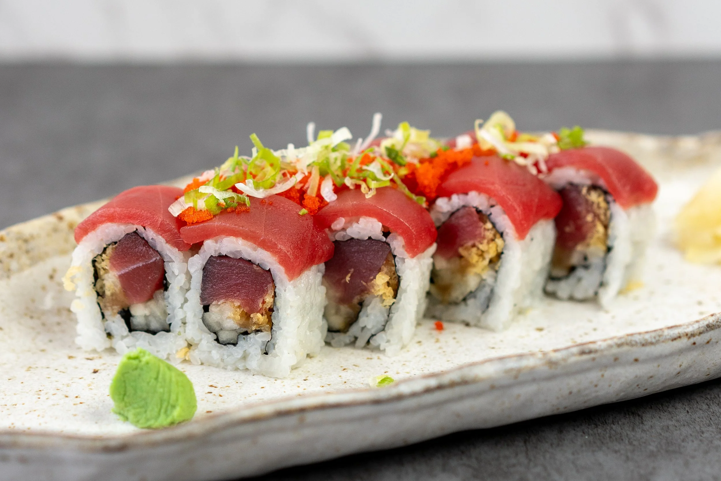 A close up macro shot of a special tuna roll. 8 piece maki sushi with tuna, crunch, cucumbers, and kampyo, topped with more tuna, tobiko (flying fish roe), and scallions.