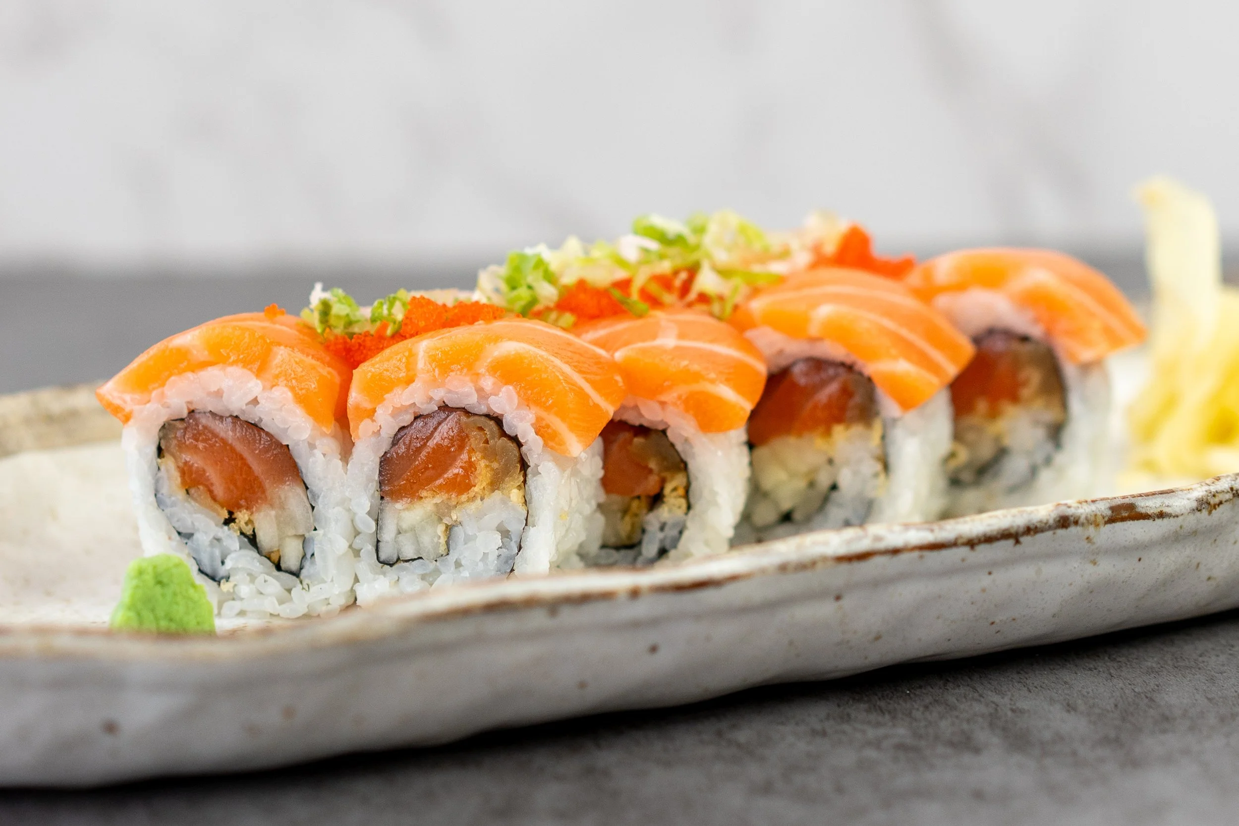 A close-up macro shot of a special roll featuring salmon. 8 piece maki sushi with salmon, crunch, cucumbers, and kampyo, topped with more salmon, tobiko (flying fish roe), and scallions.
