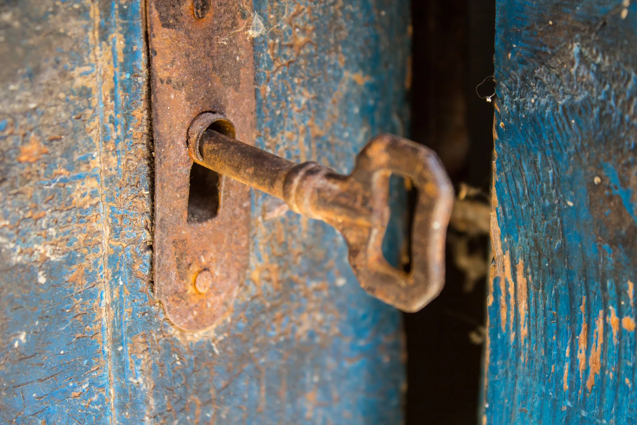 Close-up of a rusty door latch and lock on a weathered blue wooden door.