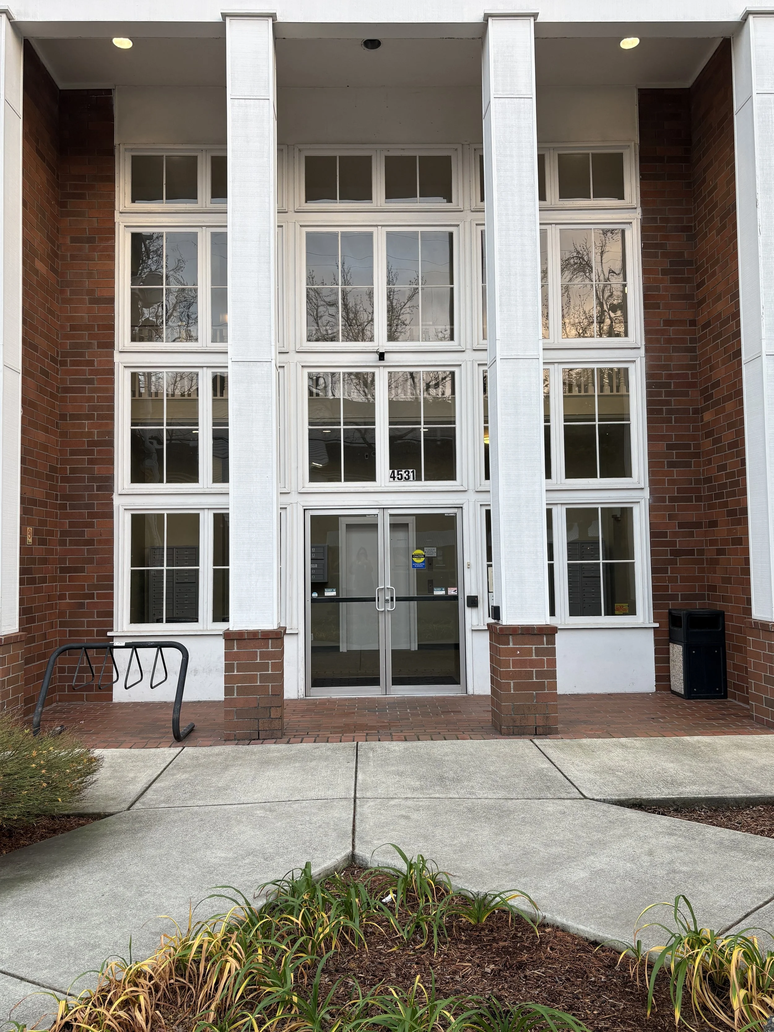 The front of the office building on 4531 SE Belmont Street which houses Laughing Fox Counseling with Fletcher Marron in Suite 205. There's a brick facade, white pillars, and a set of secure double-doors which require a code for entry.