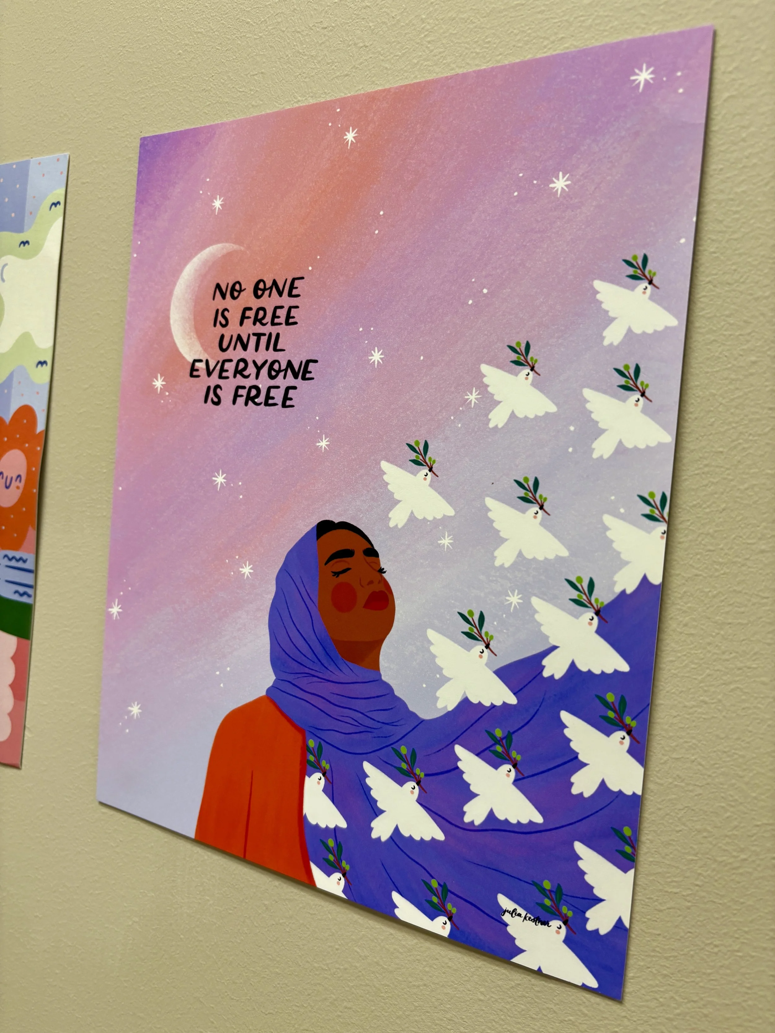 A closeup of artwork depicting a dark-skinned girl wearing a red top and purple headscarf surrounded by doves. The art says "No one is free until everyone is free."