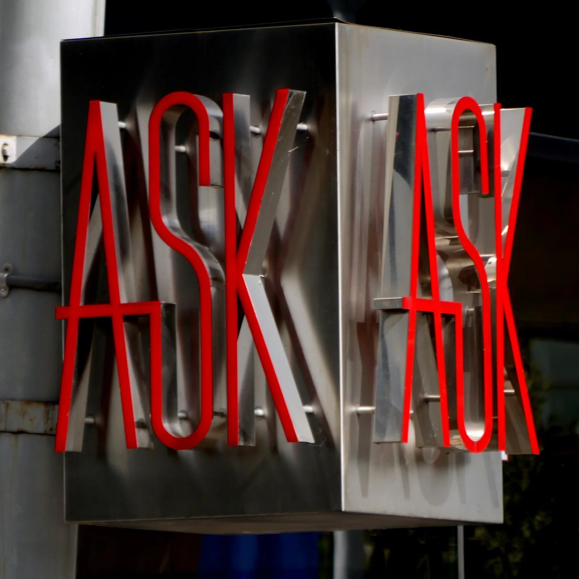 Neon sign reading 'ASK YOUR' in red letters on a metallic background.
