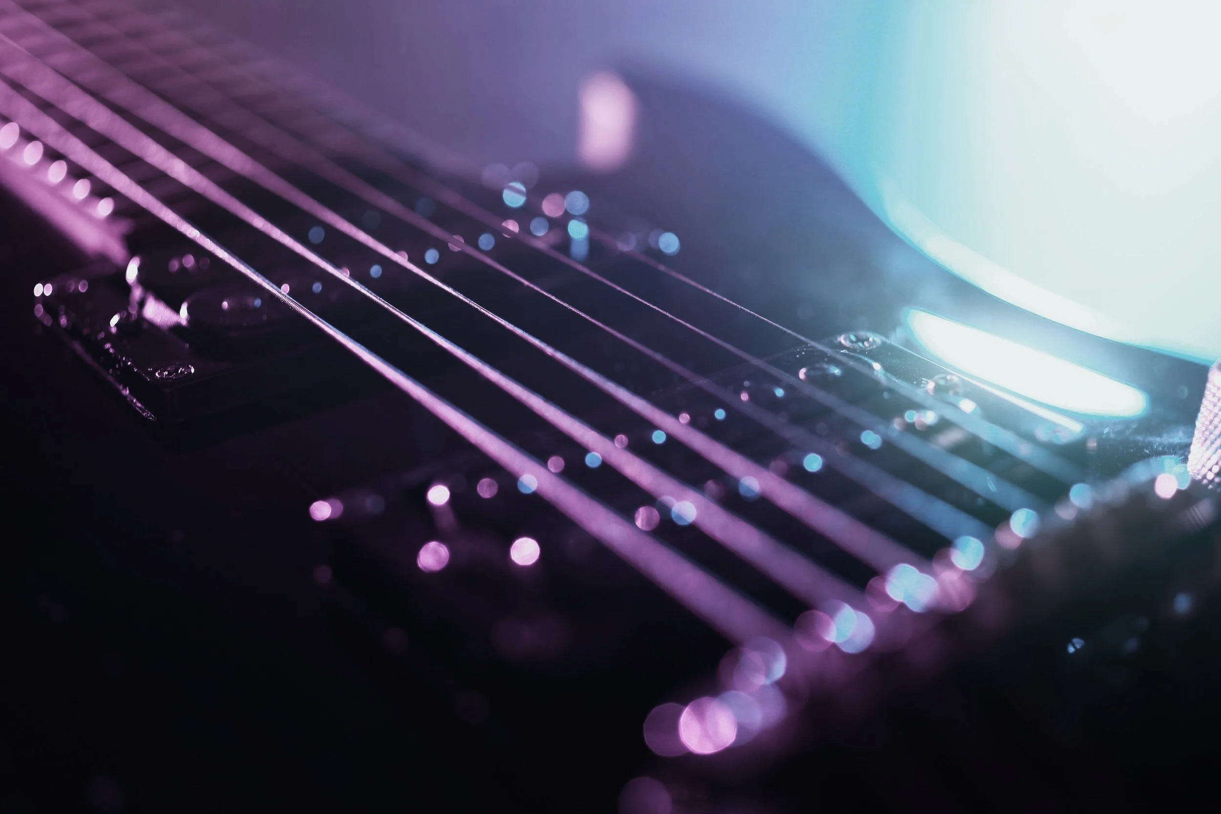 Close-up of an electric guitar neck with strings illuminated by purple and blue lighting.