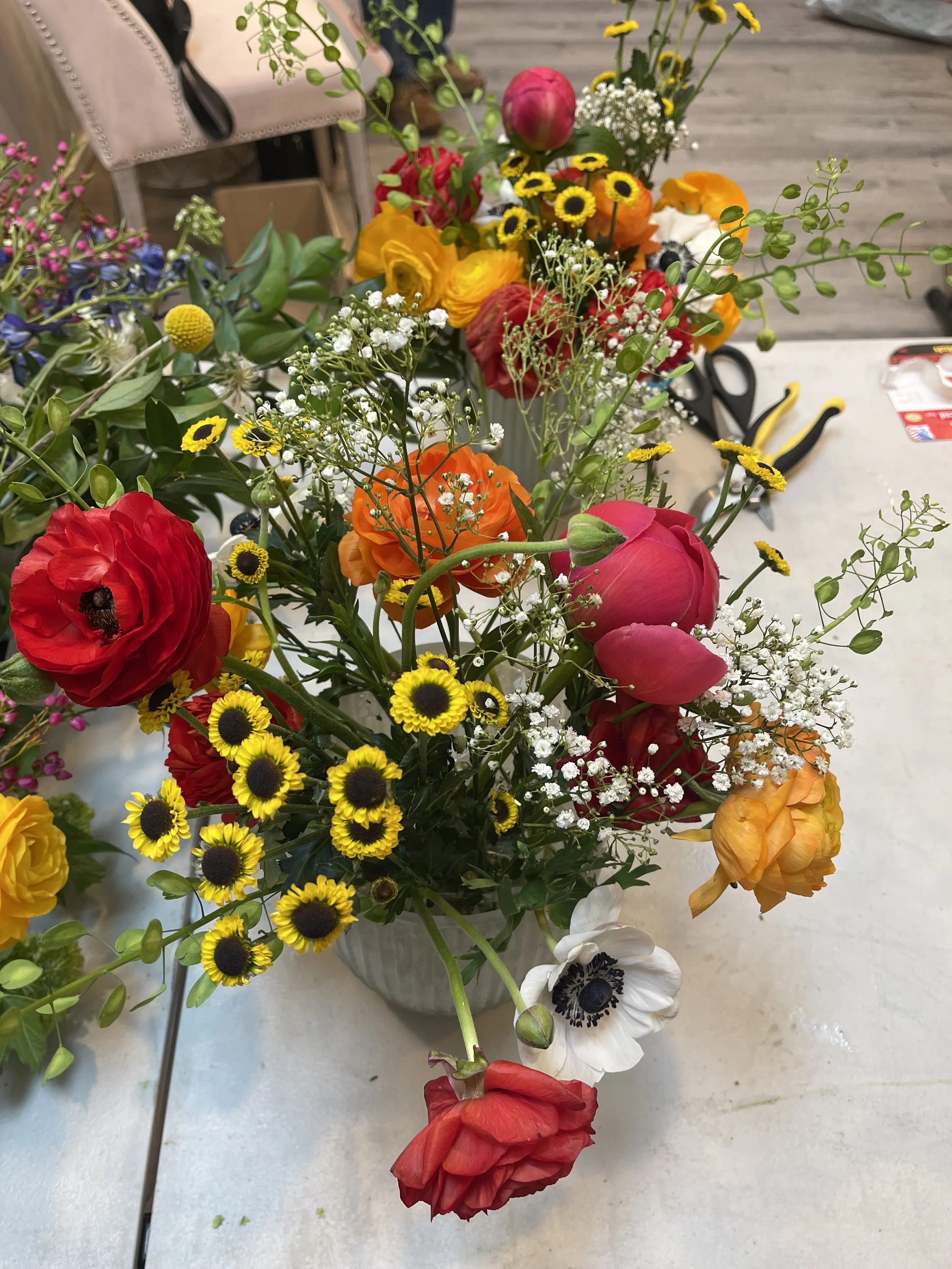 Colorful mixed flower bouquet in a vase, including poppies, daisies, ranunculus, and baby's breath, on a table.