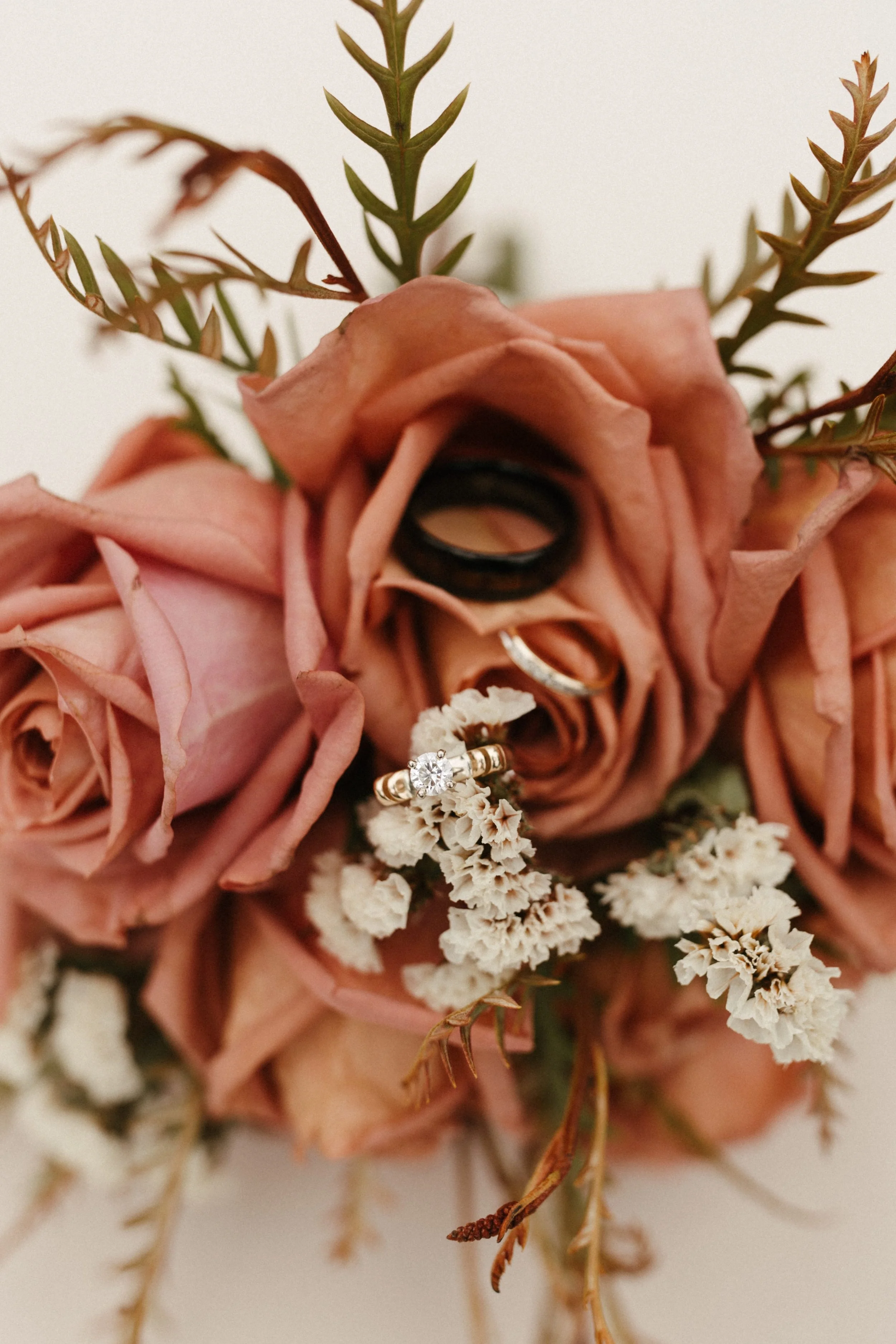 Close-up of a wedding bouquet with pink roses, white flowers, greenery, and wedding rings.