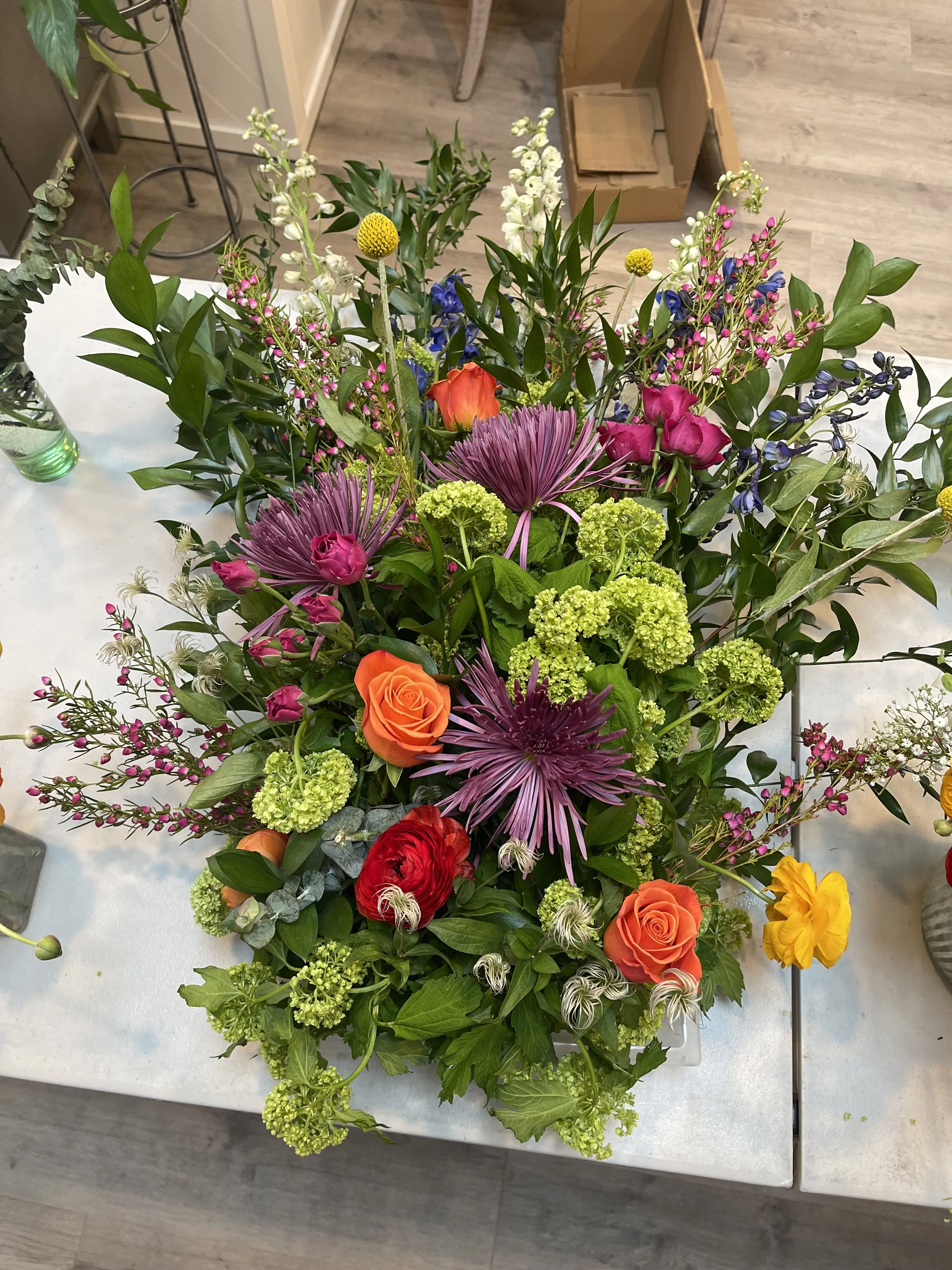 Colorful flower arrangement with roses, chrysanthemums, hydrangeas, and greenery on a white table.