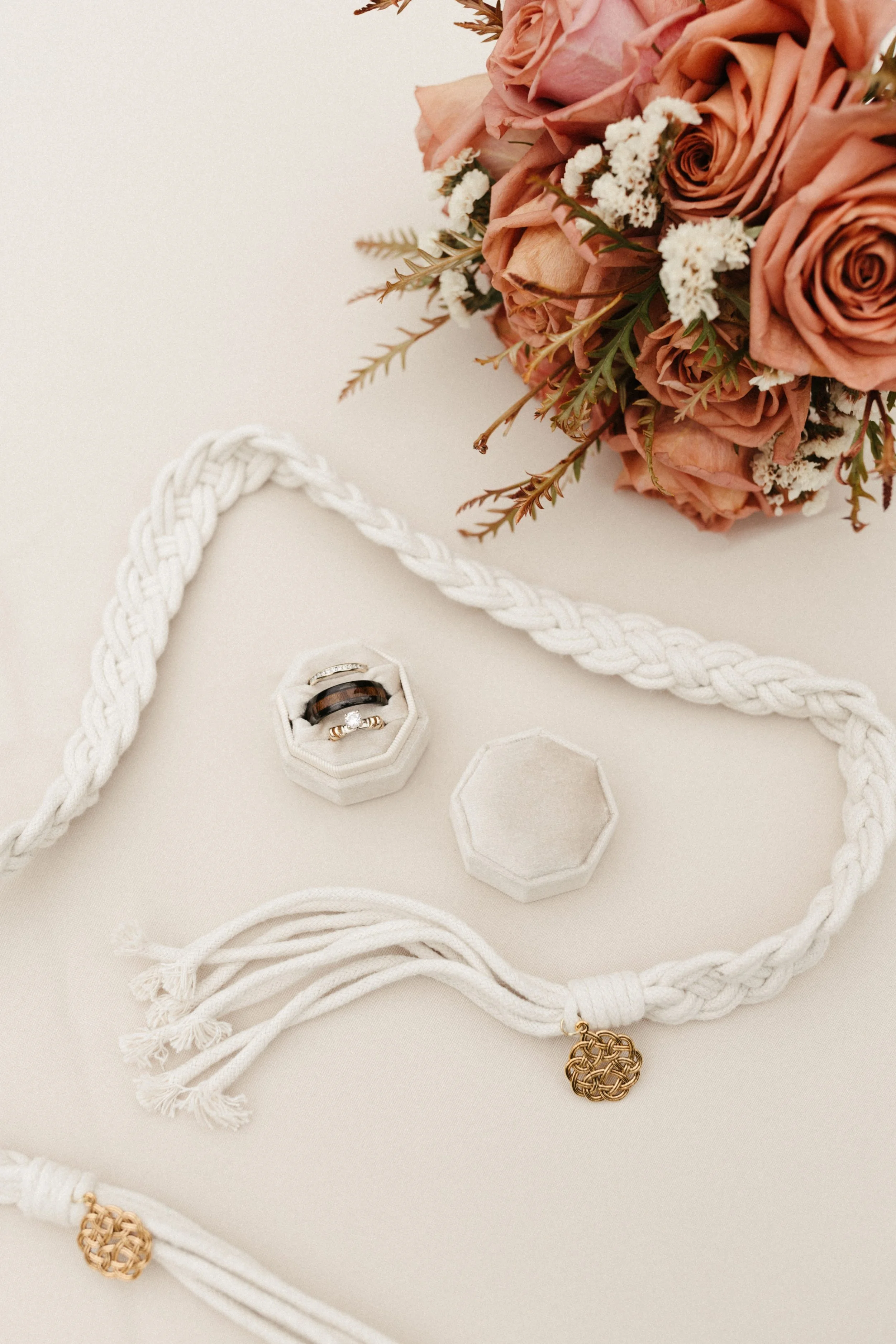 A bouquet of pink roses and white flowers, along with a necklace, rings, and jewelry box on a white surface.