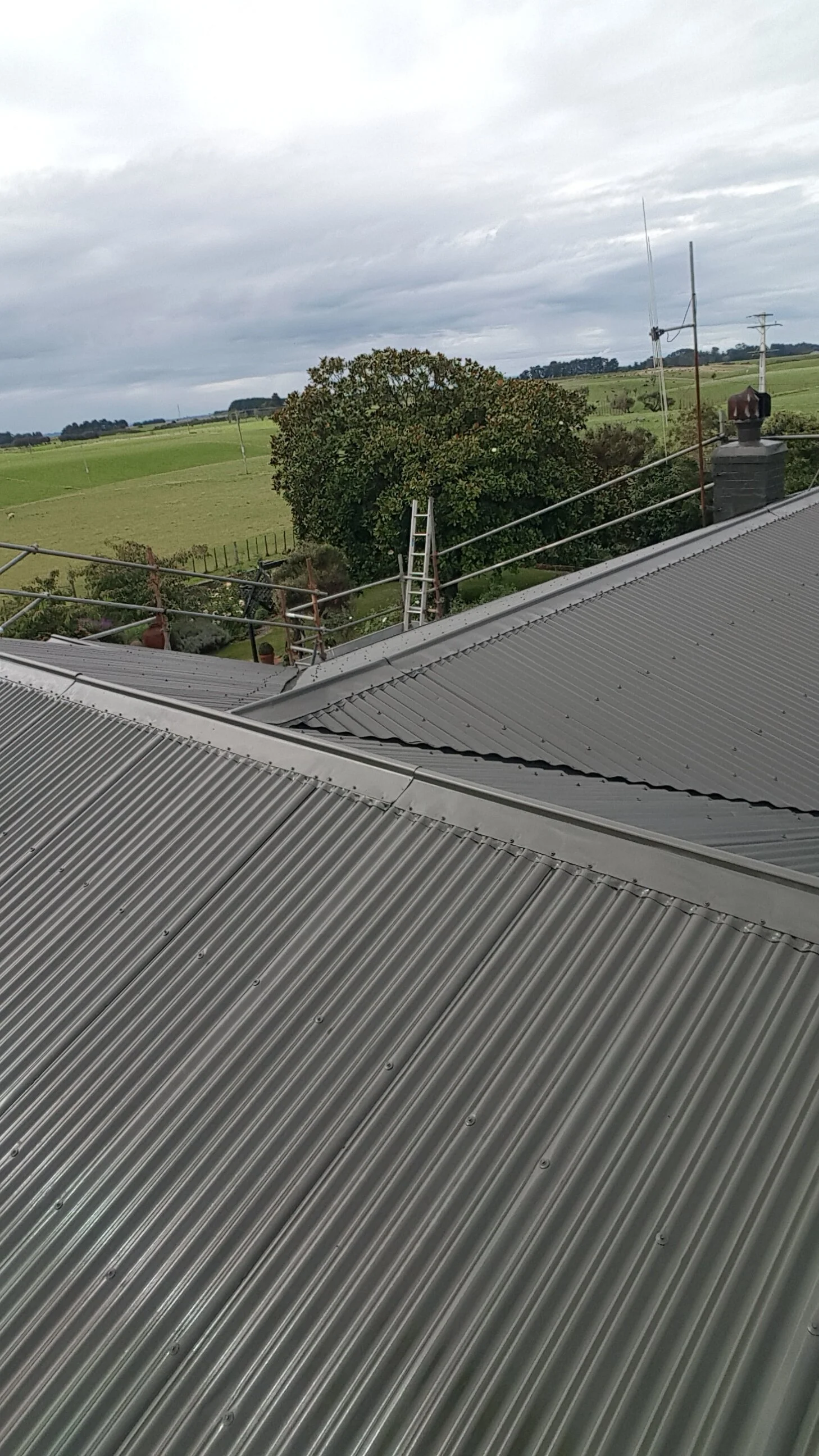 Metal roof with skylight and surrounding rural landscape with green fields, trees, power lines, and cloudy sky.