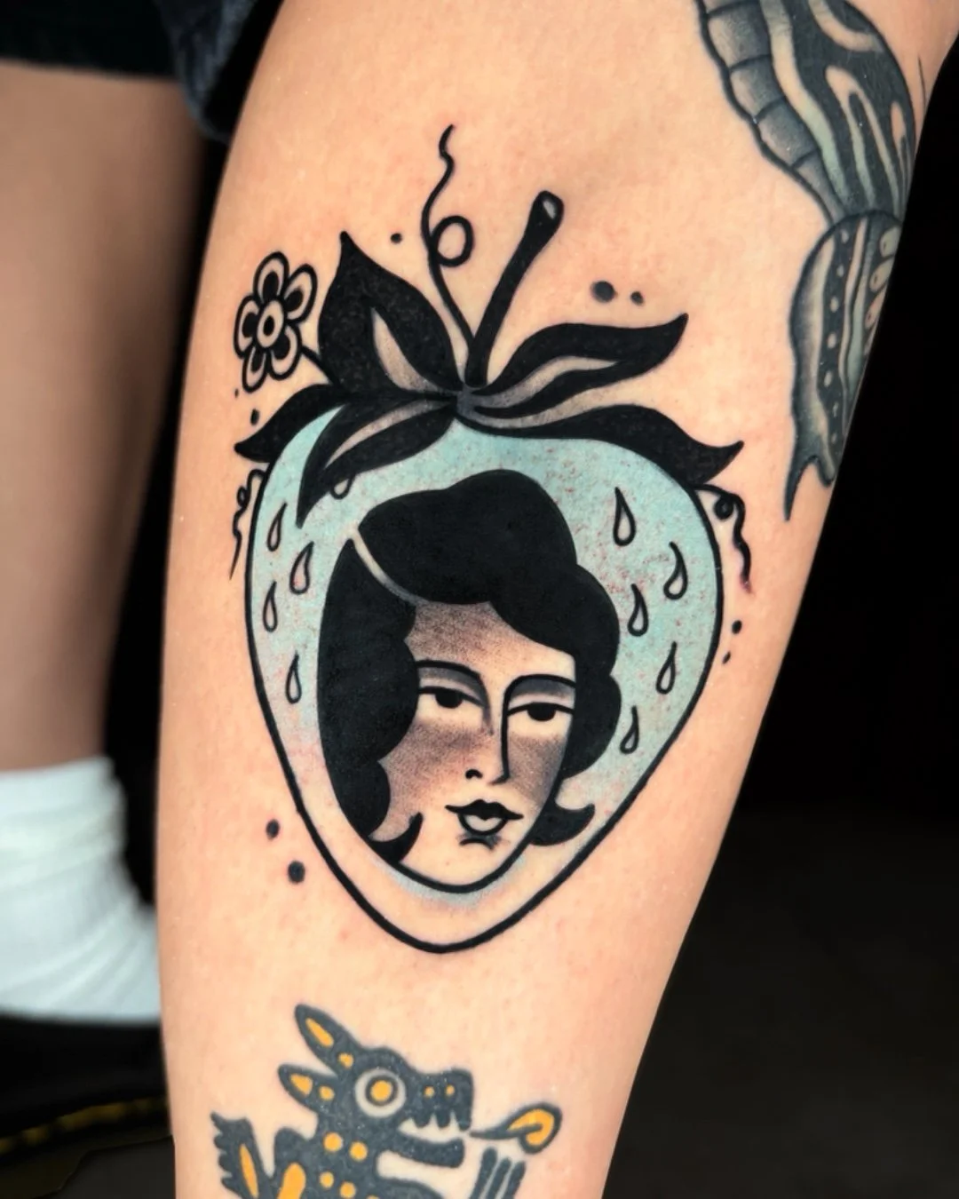 American traditional strawberry tattoo done in West Palm Beach, Florida. This custom tattoo features a stylized strawberry with a feminine face, created with bold outlines, strong contrast, and classic American traditional aesthetics. Tattooed by Flo