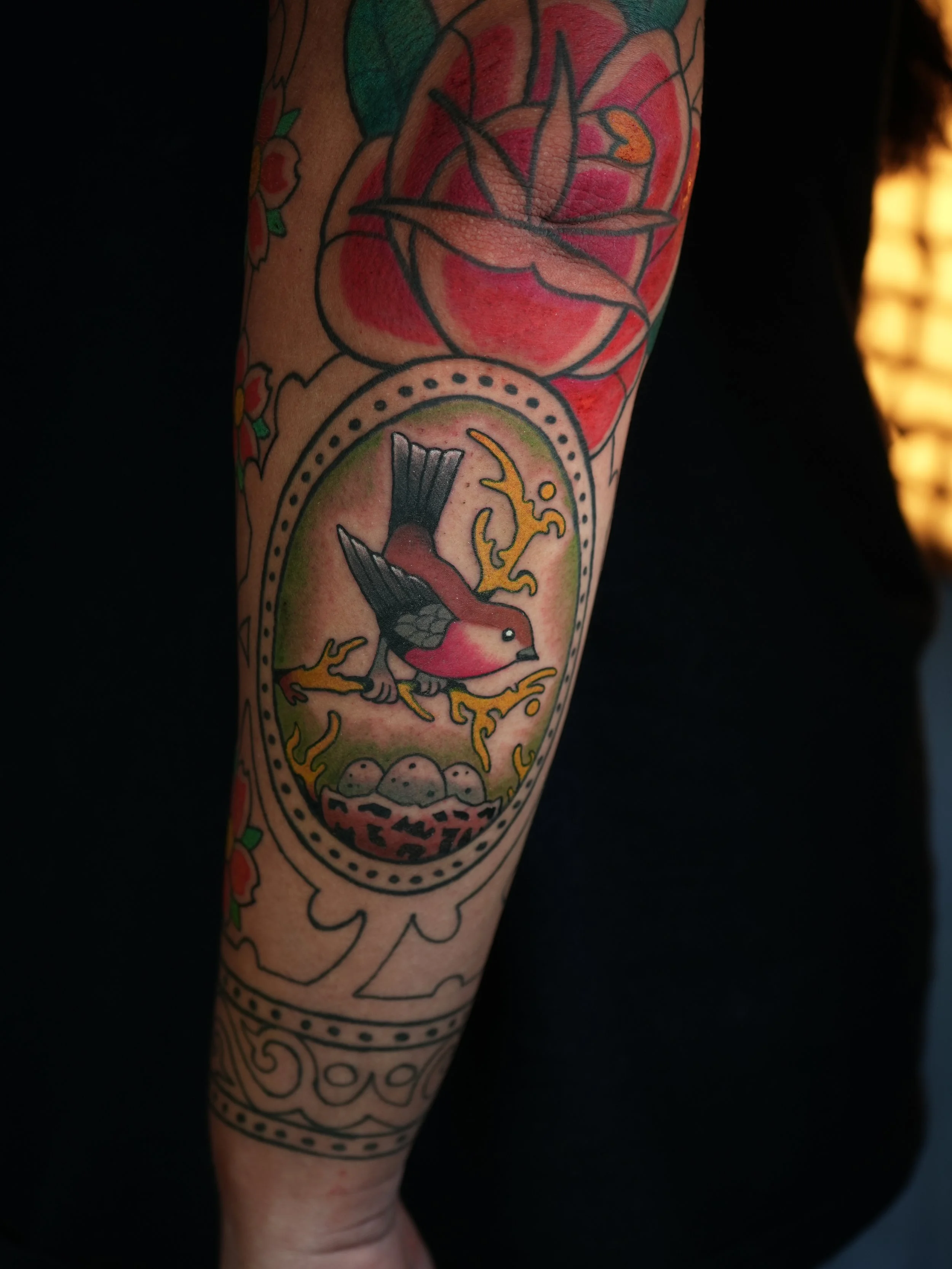 Colorful Traditional bird tattoo on the forearm featuring a bird protecting its nest with eggs, surrounded by ornamental details, created by Kappa in West Palm Beach, Florida.