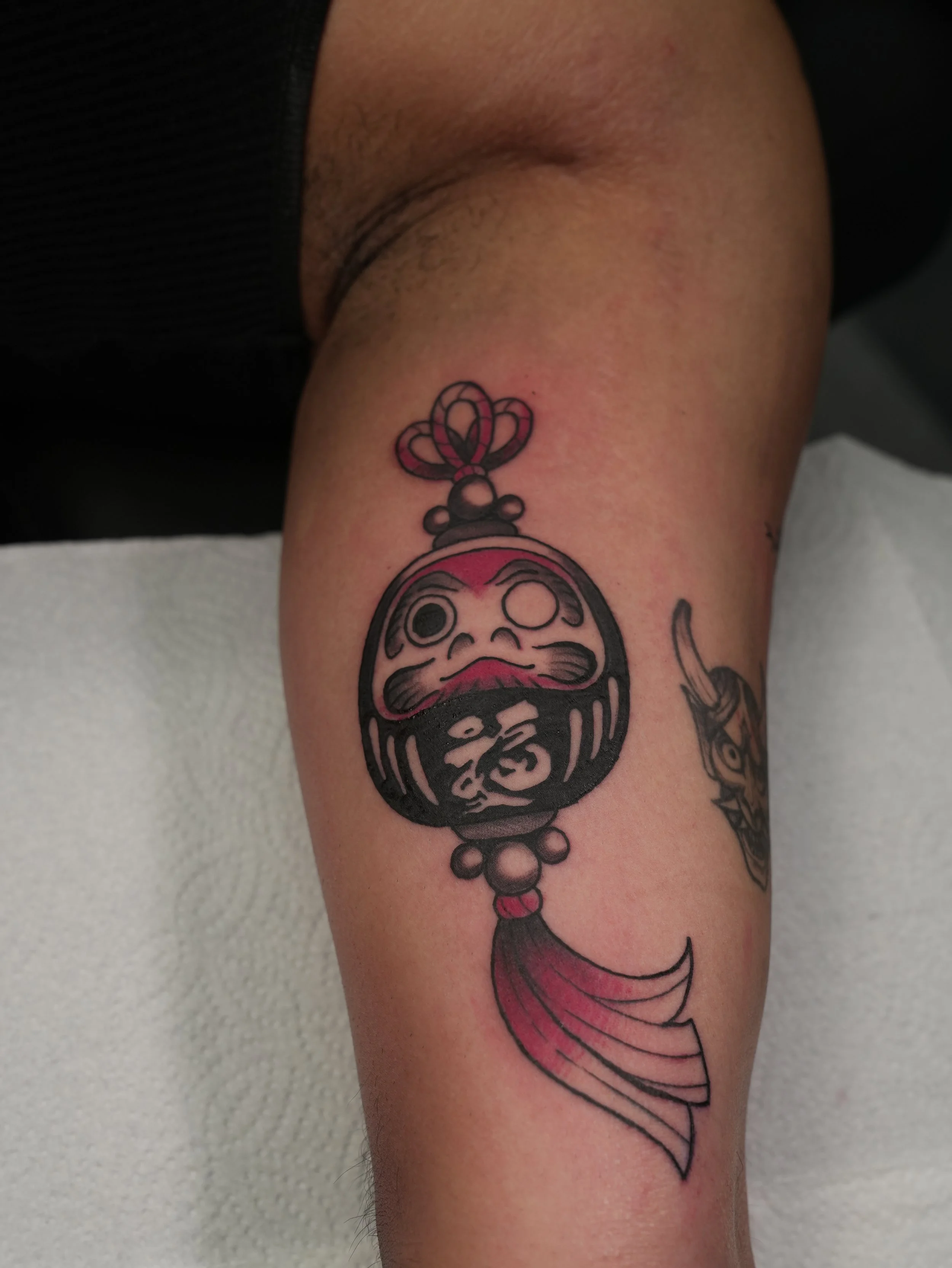 Japanese-inspired Daruma lantern tattoo on the forearm featuring bold black outlines, red accents, and traditional ornamental details, created by Kappa in West Palm Beach, Florida.