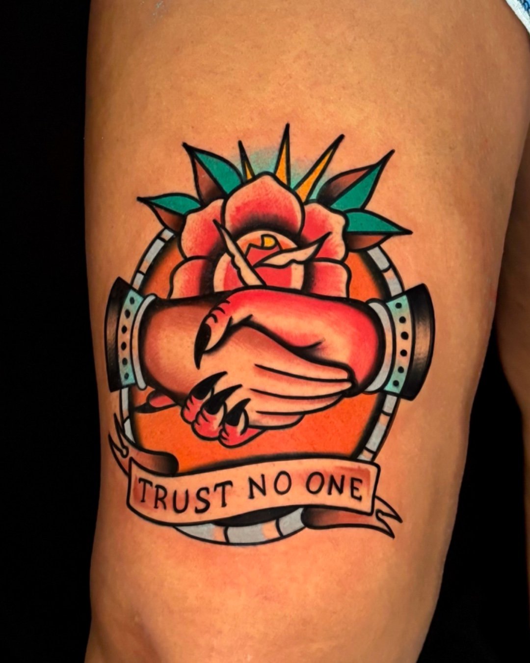 American Traditional tattoo Trust no One West Palm Beach, Florida, featuring a classic rose embraced by clasped hands and a banner that reads “Trust No One.” This traditional tattoo design represents loyalty, trust, and self-protection, executed with