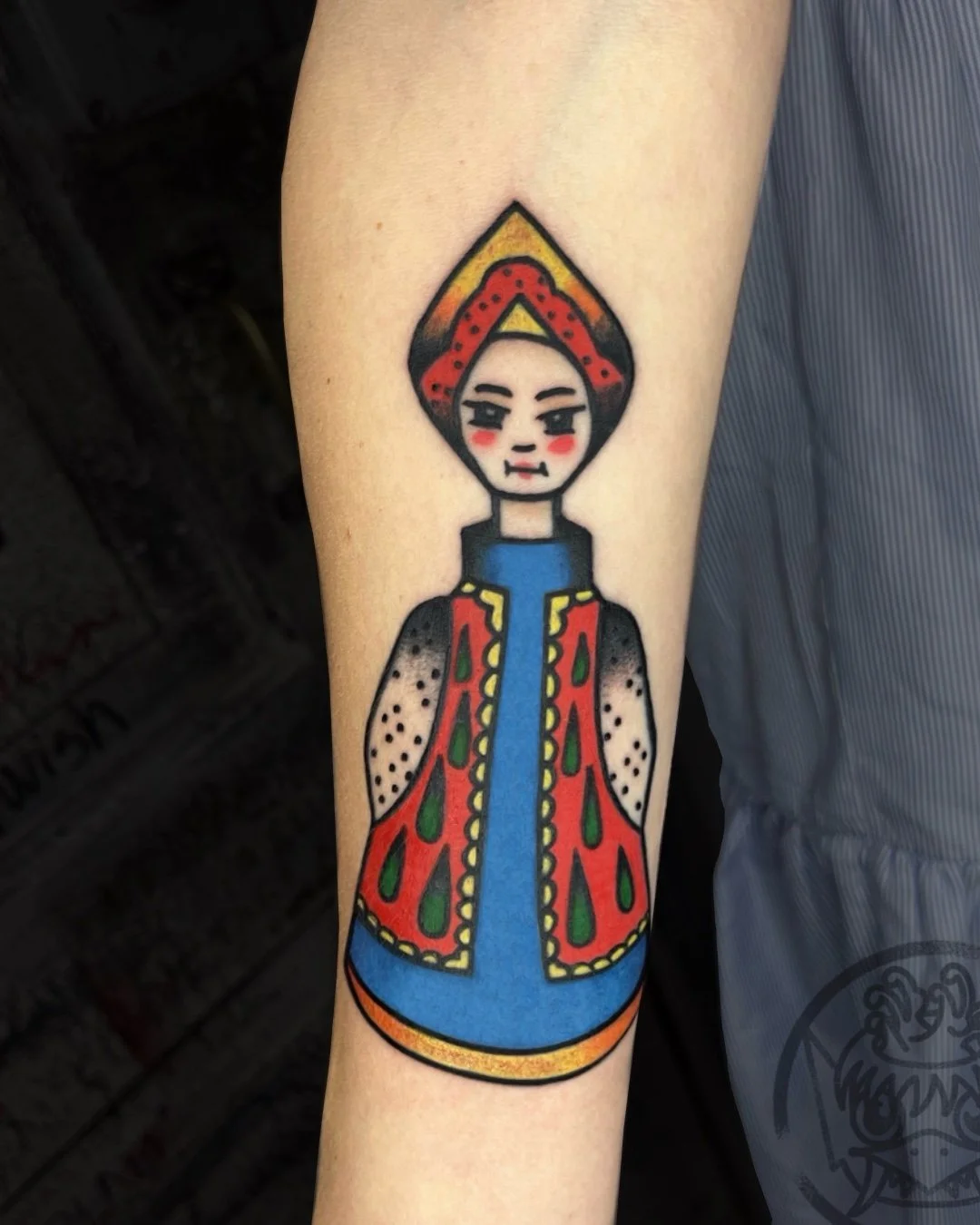American traditional doll tattoo done in West Palm Beach, Florida. This custom tattoo features a stylized folk-inspired doll, created with bold outlines, solid color saturation, and a balanced composition rooted in American traditional tattoo aesthet