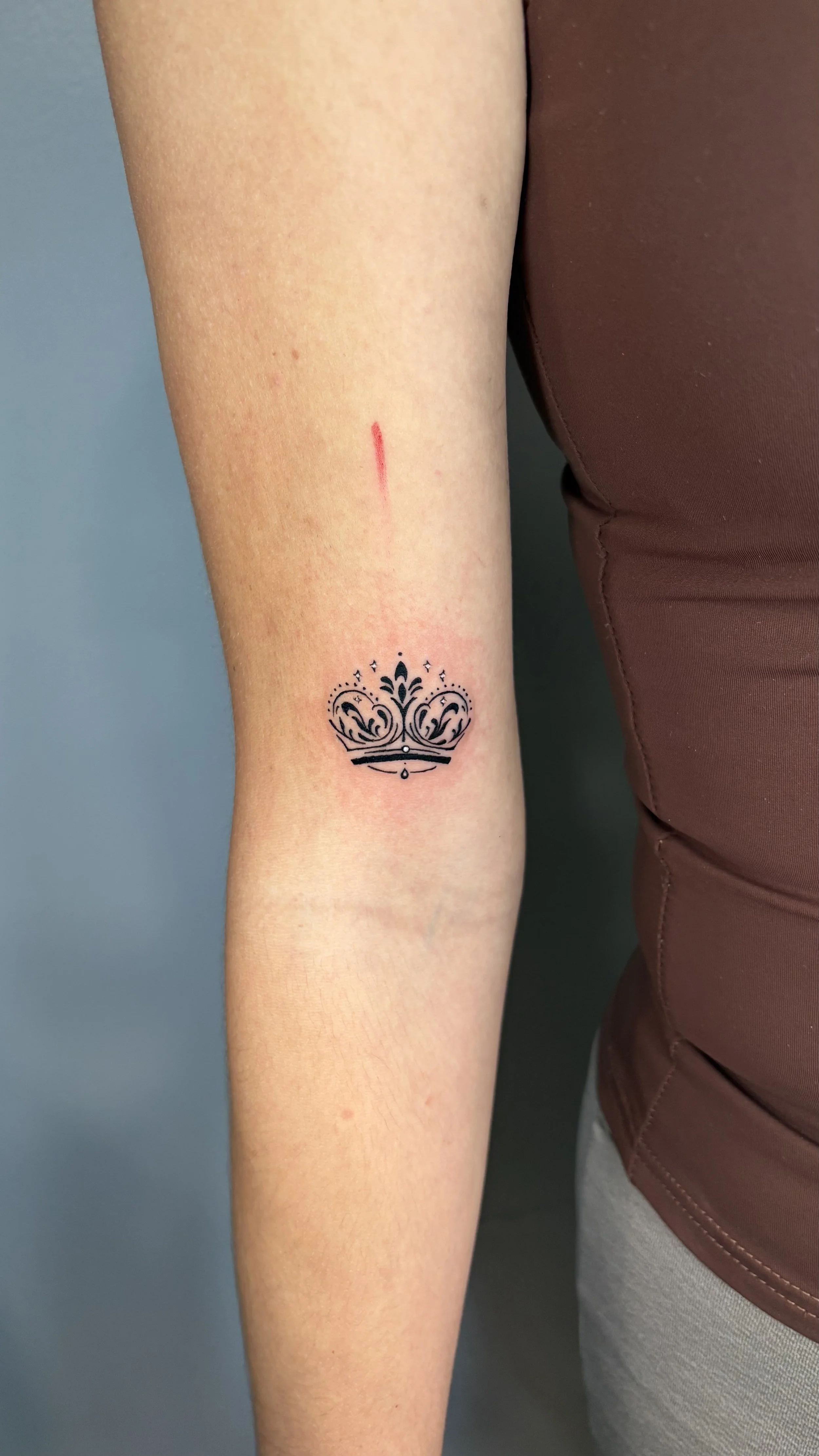Fine line crown tattoo with delicate details, tattooed on the forearm by Flow Kappa in West Palm Beach, Florida.